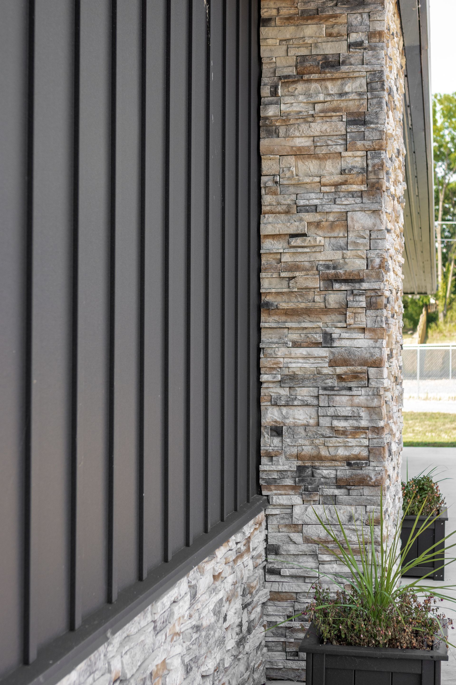 Gray vertical siding next to a stone pillar and a dark planter box with plants.