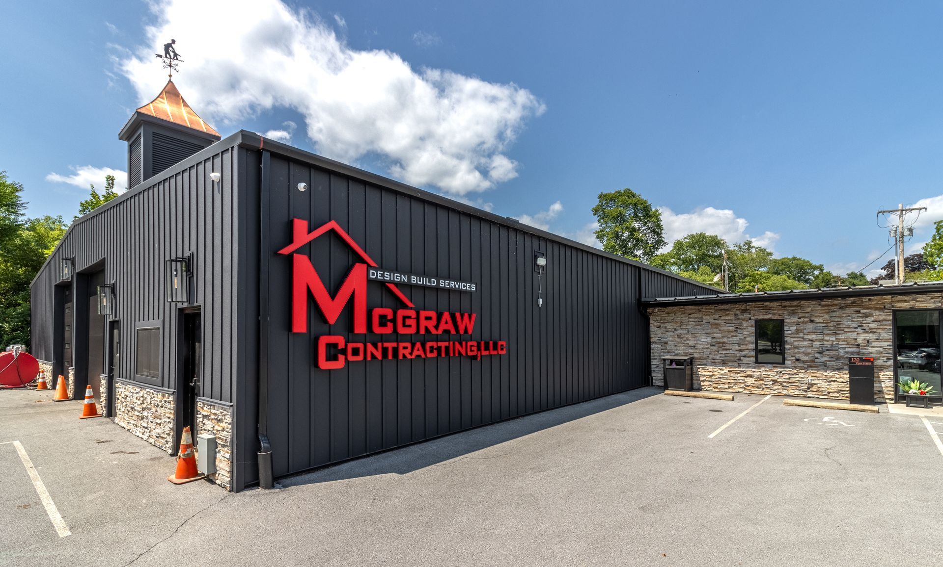 McGraw Contracting LLC building, black metal siding, red logo, stone facade, sunny day.