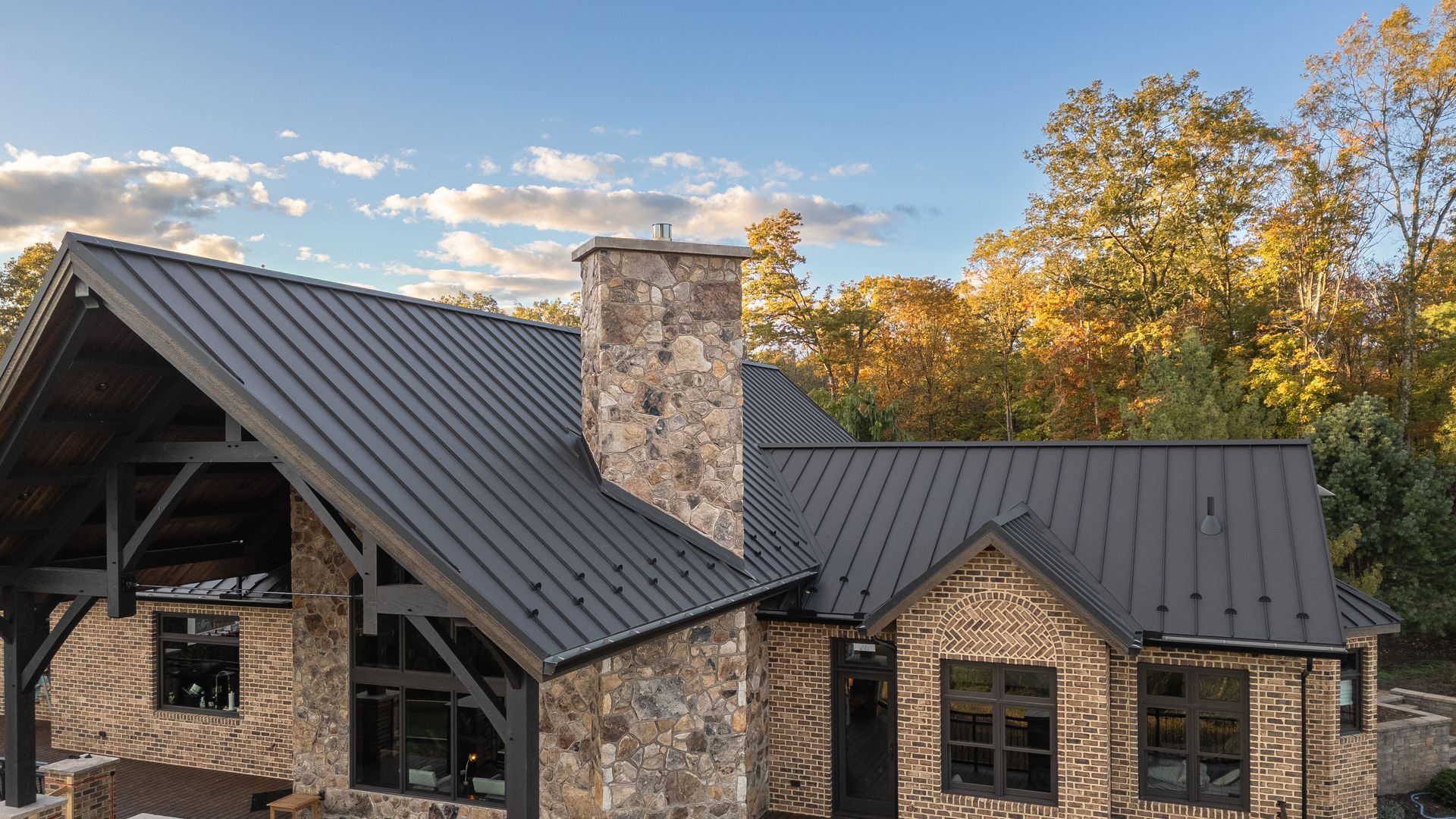 Stone cabin with dark metal roof, chimney, and fall foliage.
