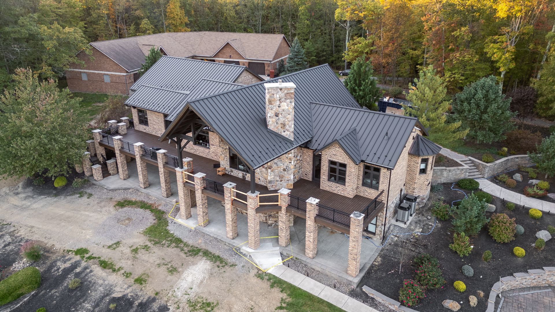 Stone house with black roof, columns, and decks, surrounded by trees.