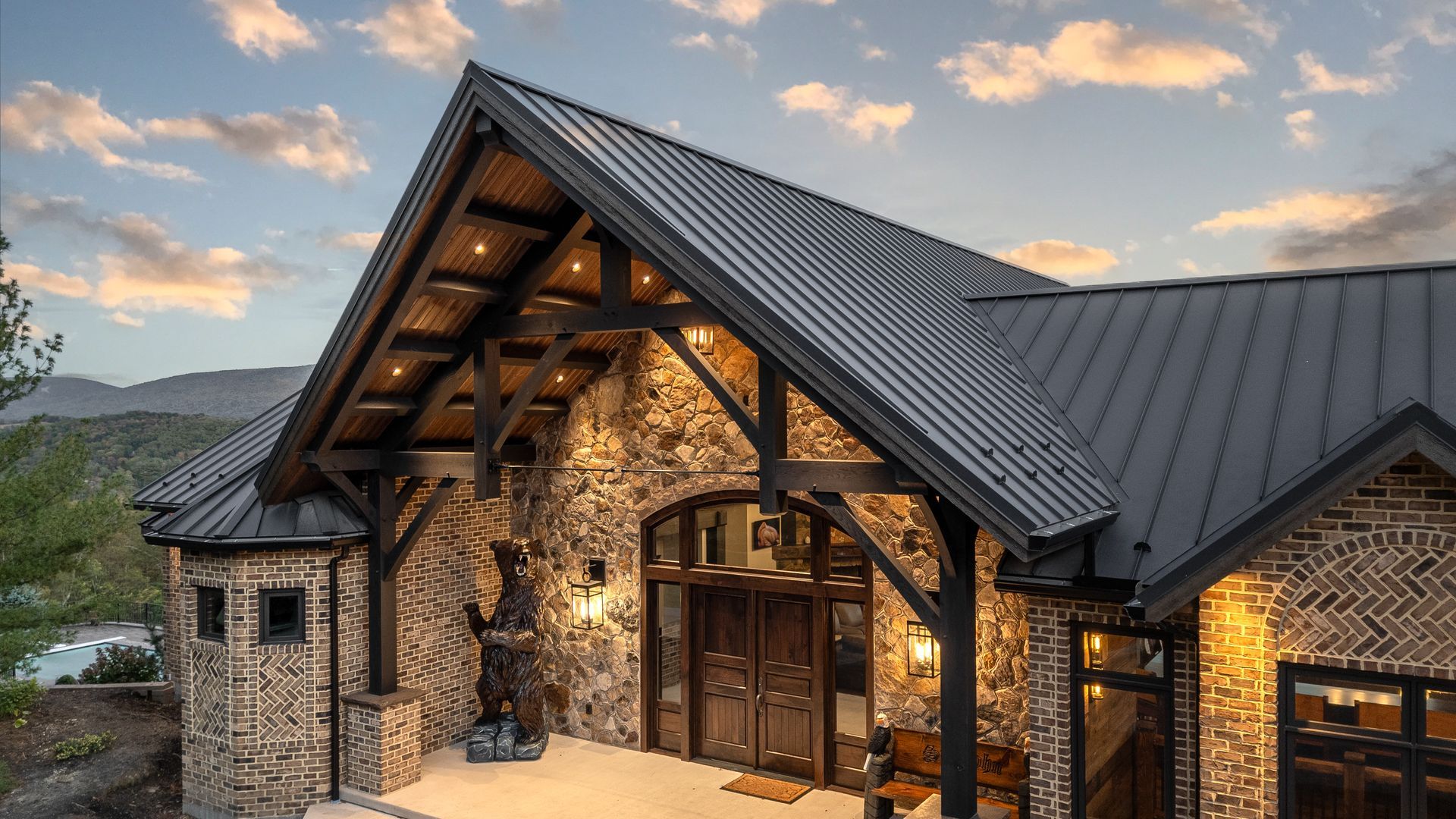 Stone and timber lodge with a dark roof, warmly lit entrance, and mountain backdrop.
