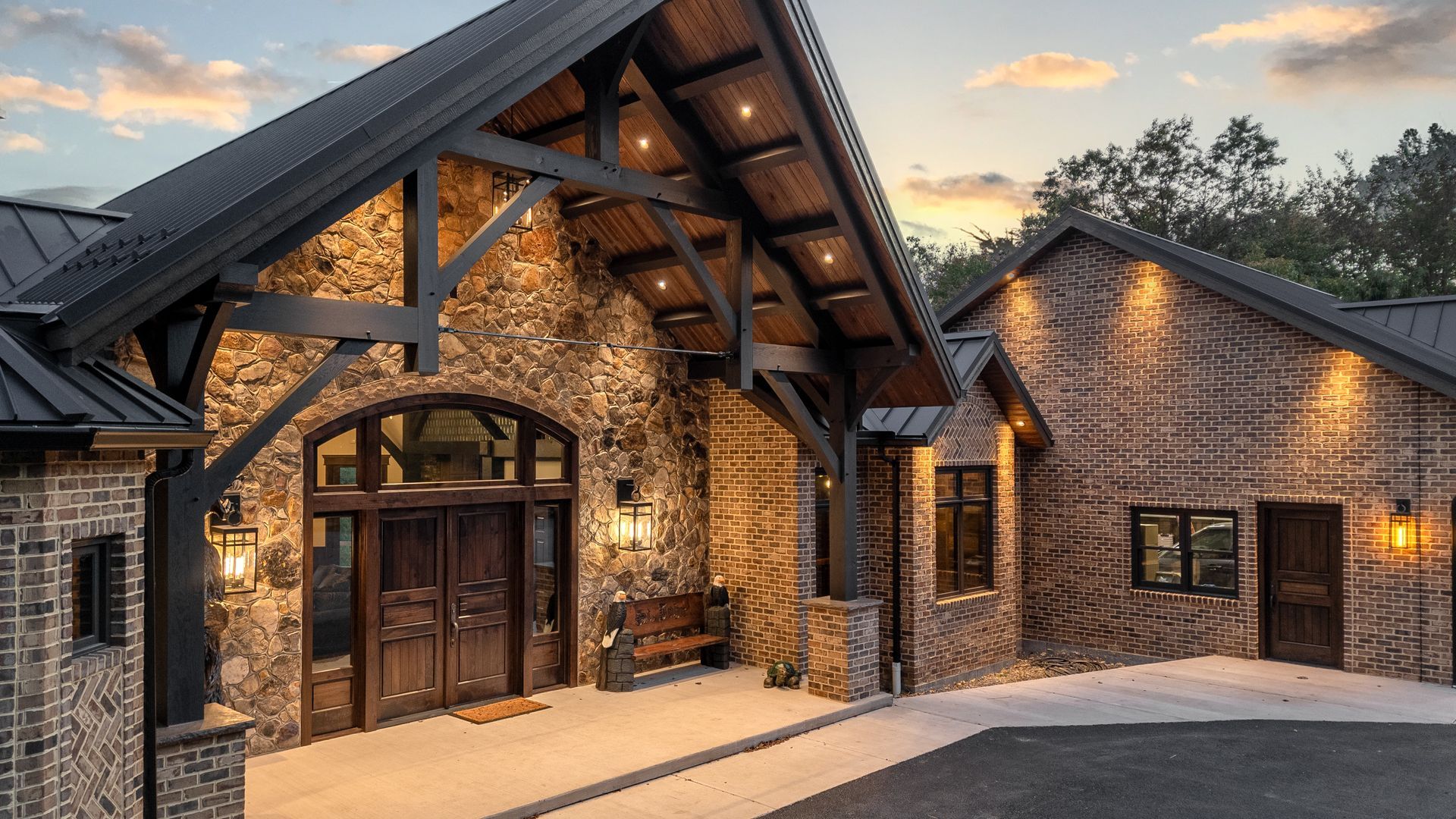 Stone and wood exterior of a house with a covered entrance and dark metal roof, lit with warm lights.