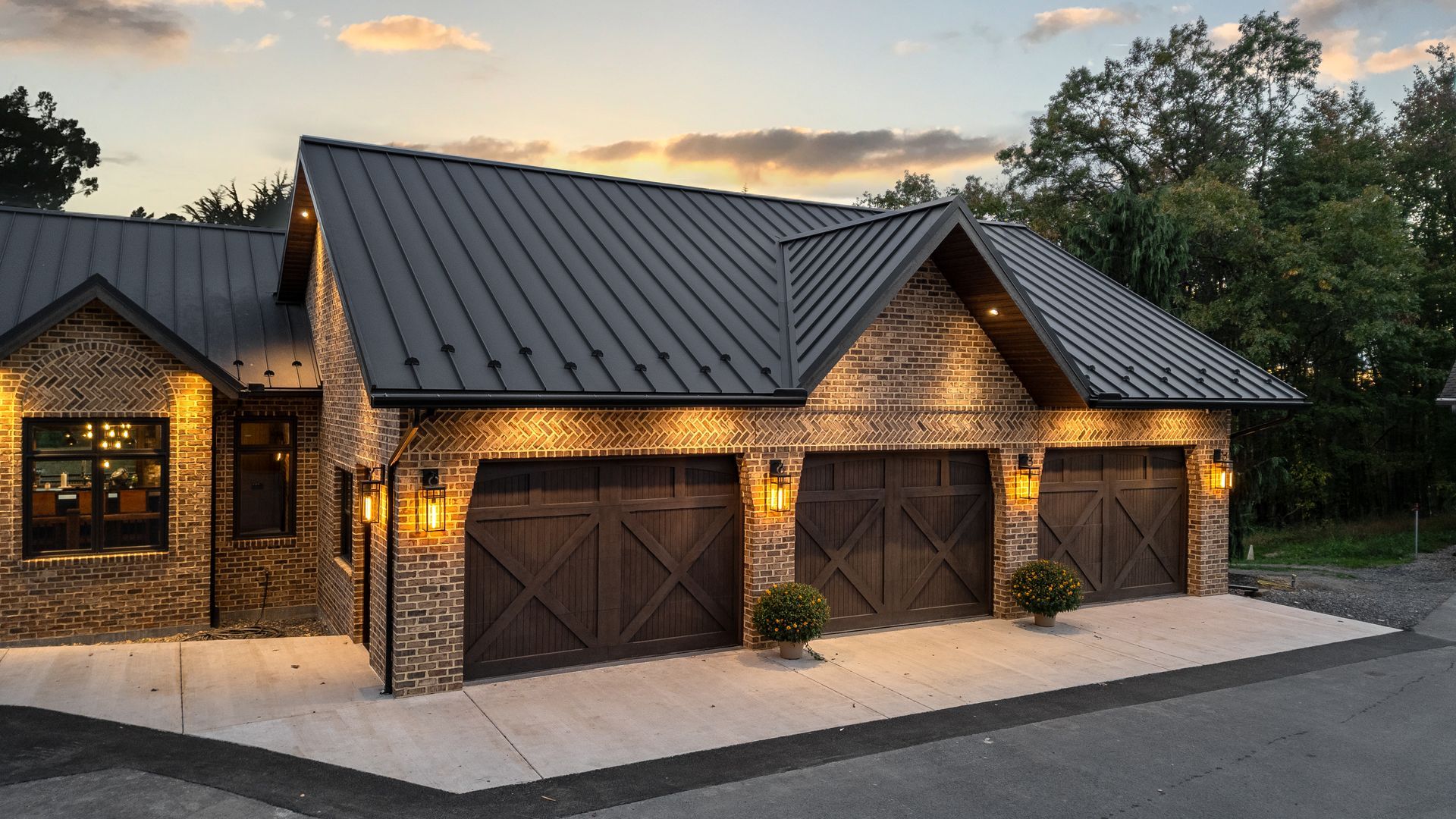 Stone garage with three dark wooden doors, black roof, and outdoor lighting.