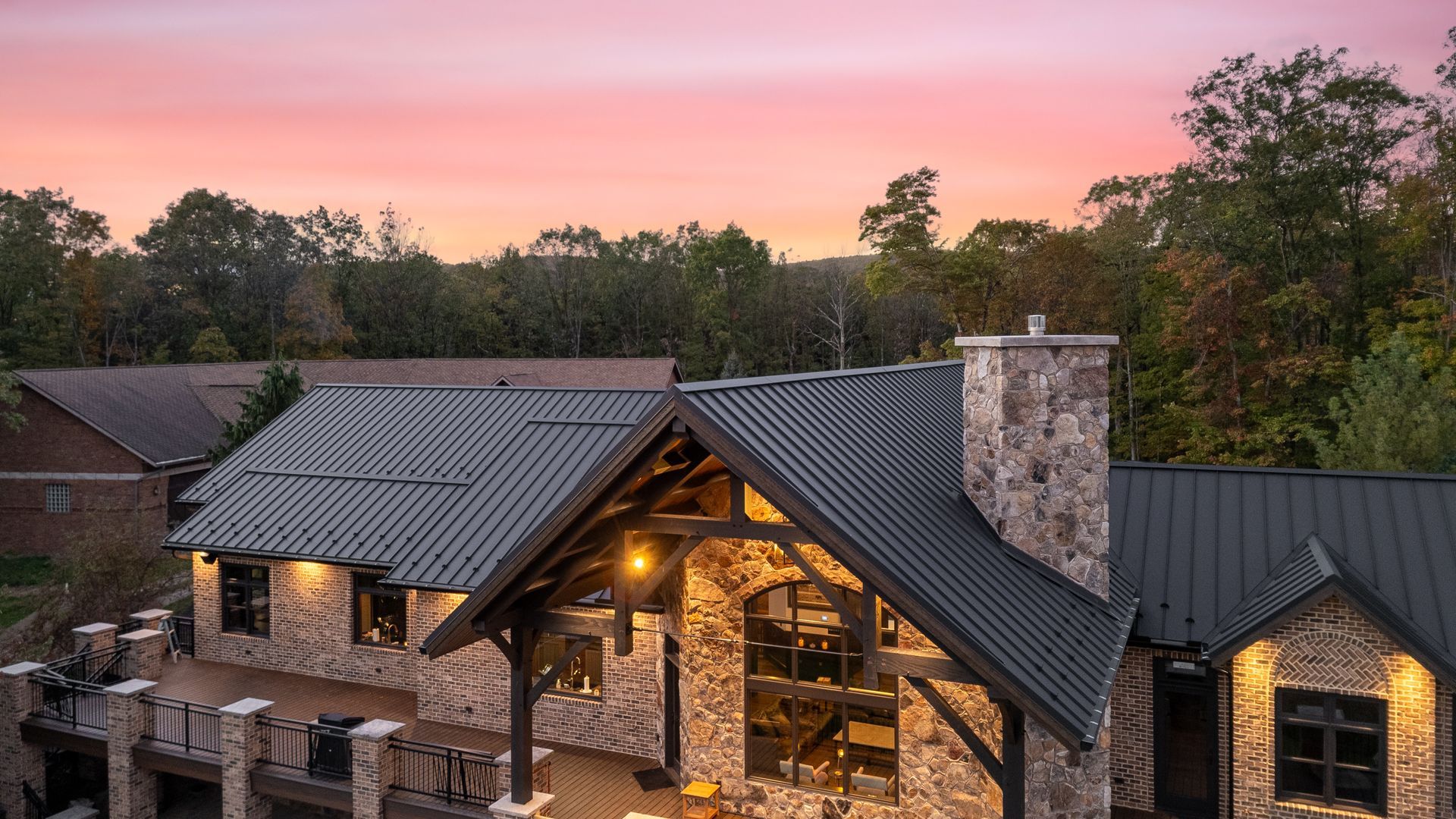 Rustic home exterior at sunset, stone and wood facade, dark roof, pink and orange sky.