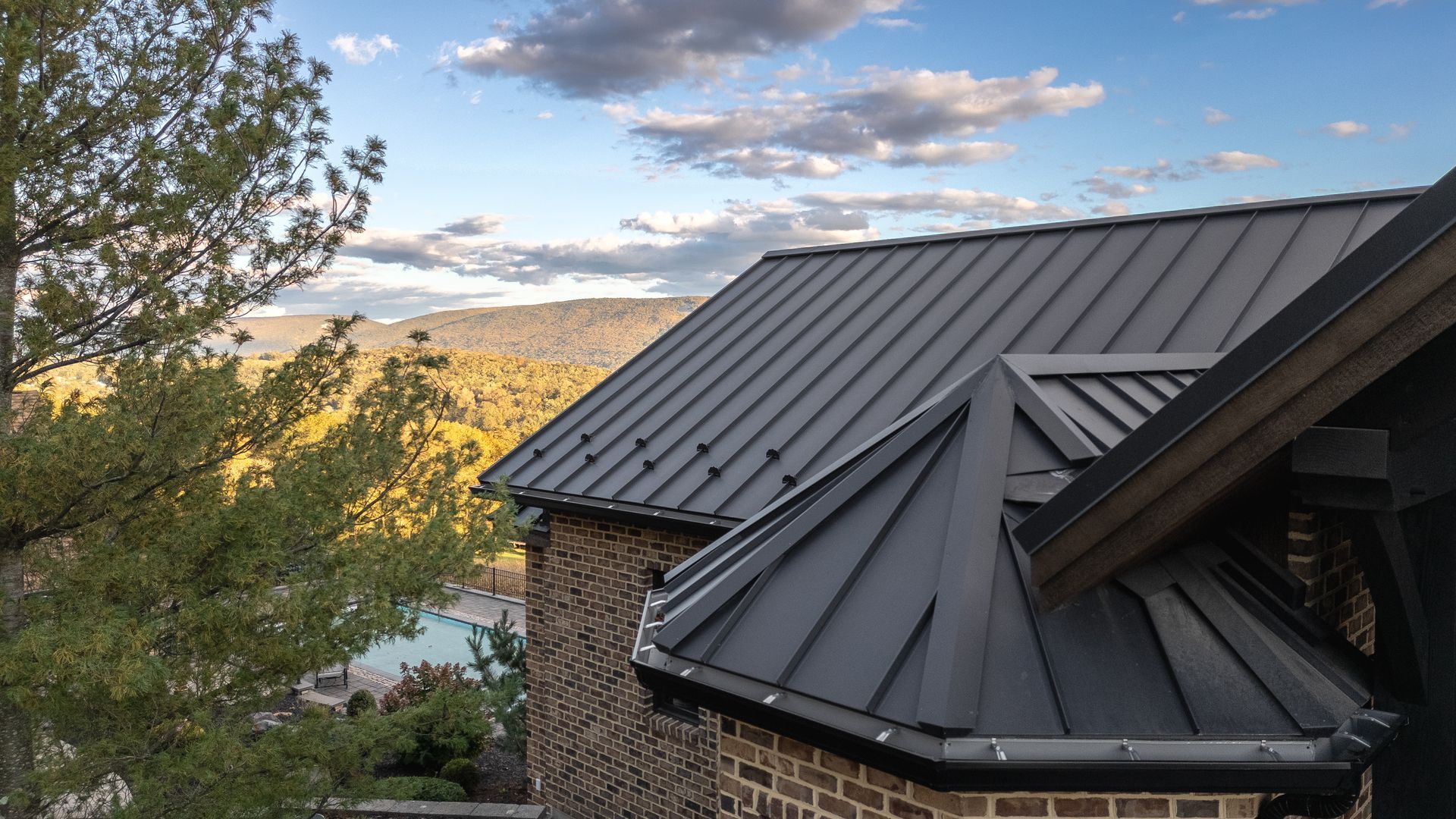 Black metal roof on a brick building against a backdrop of a mountain and cloudy sky.