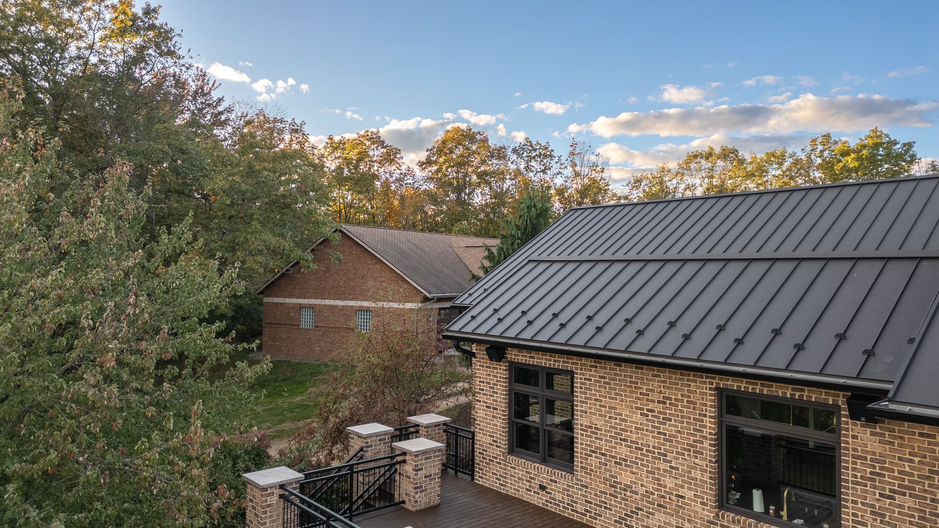 Brick buildings with dark roof against a blue sky with trees.
