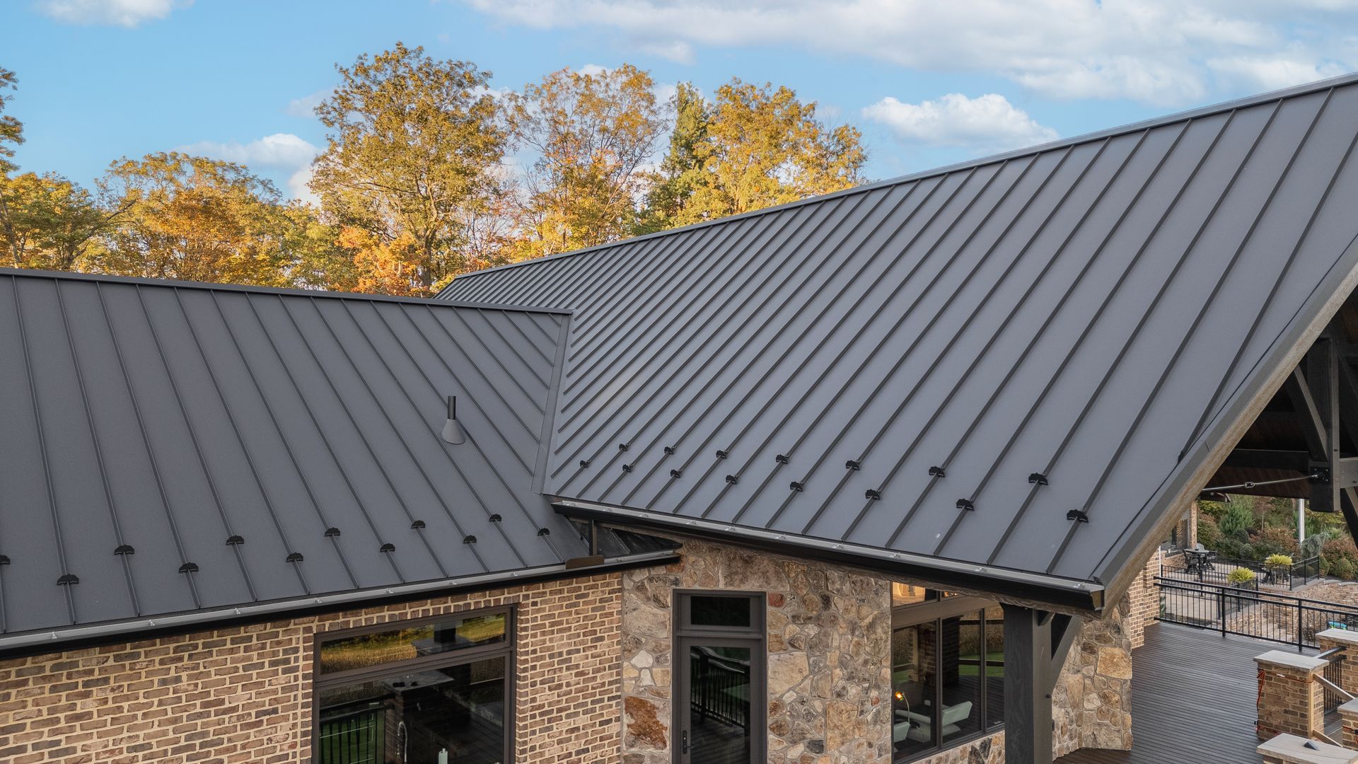 Dark gray metal roof on a stone building with trees in the background.
