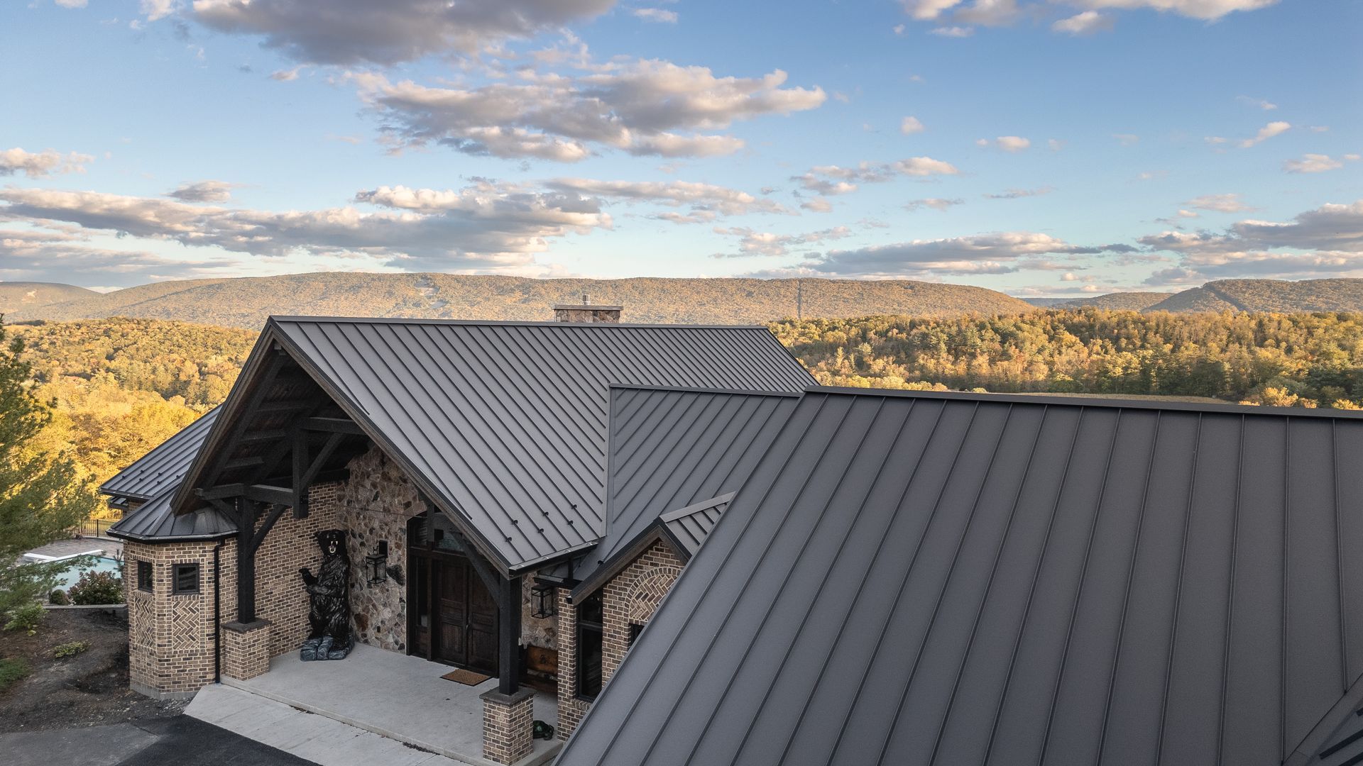 Building with metal roof, stone facade, mountains and sky in background.