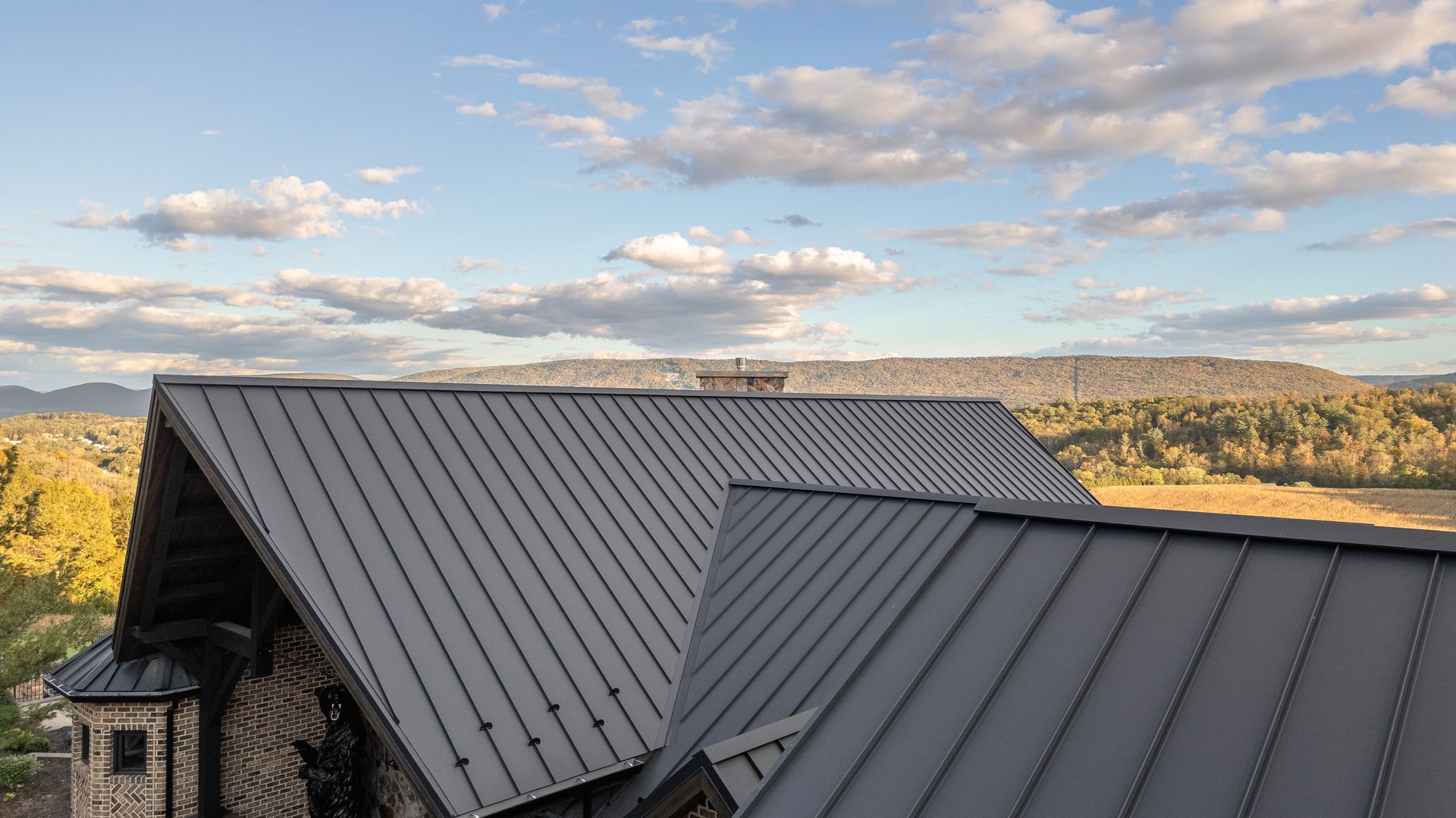 Dark gray metal roofs on a building with a mountainous backdrop and cloudy sky.