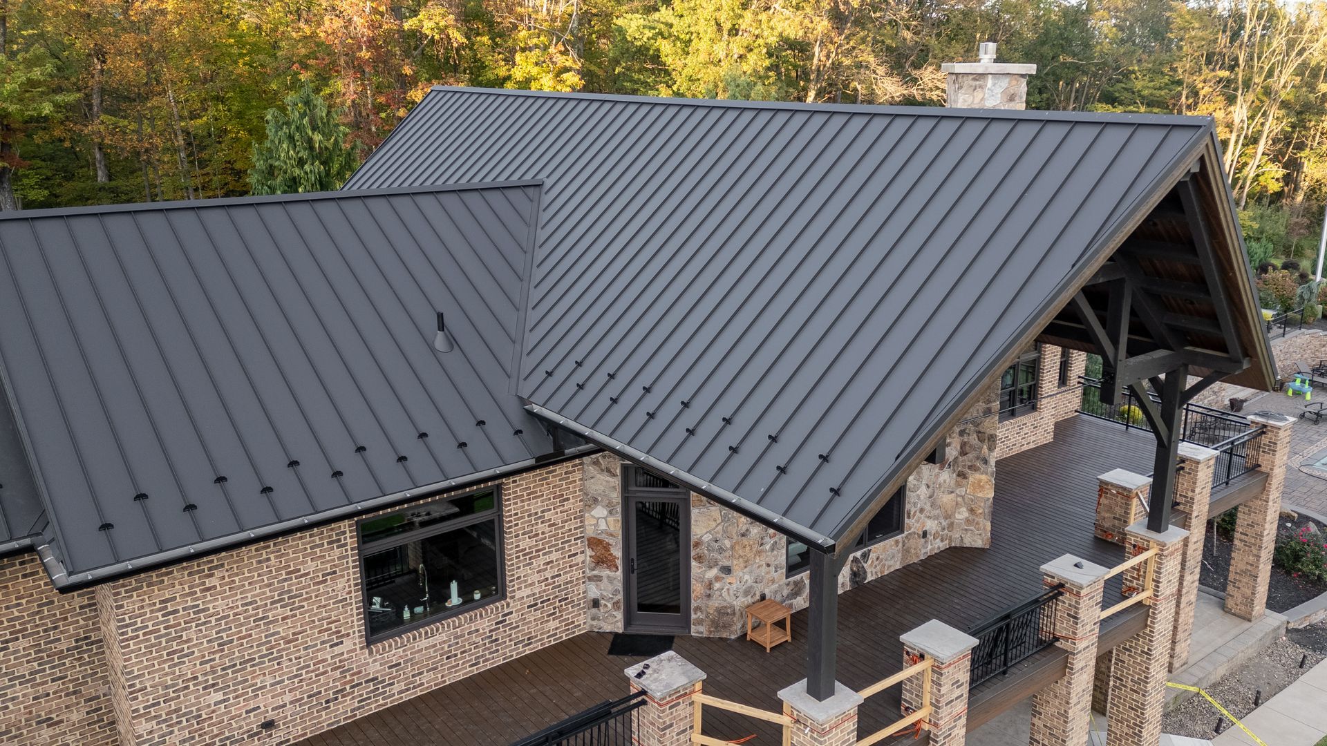 A modern house with a dark metal roof, stone facade, and a wooden porch.