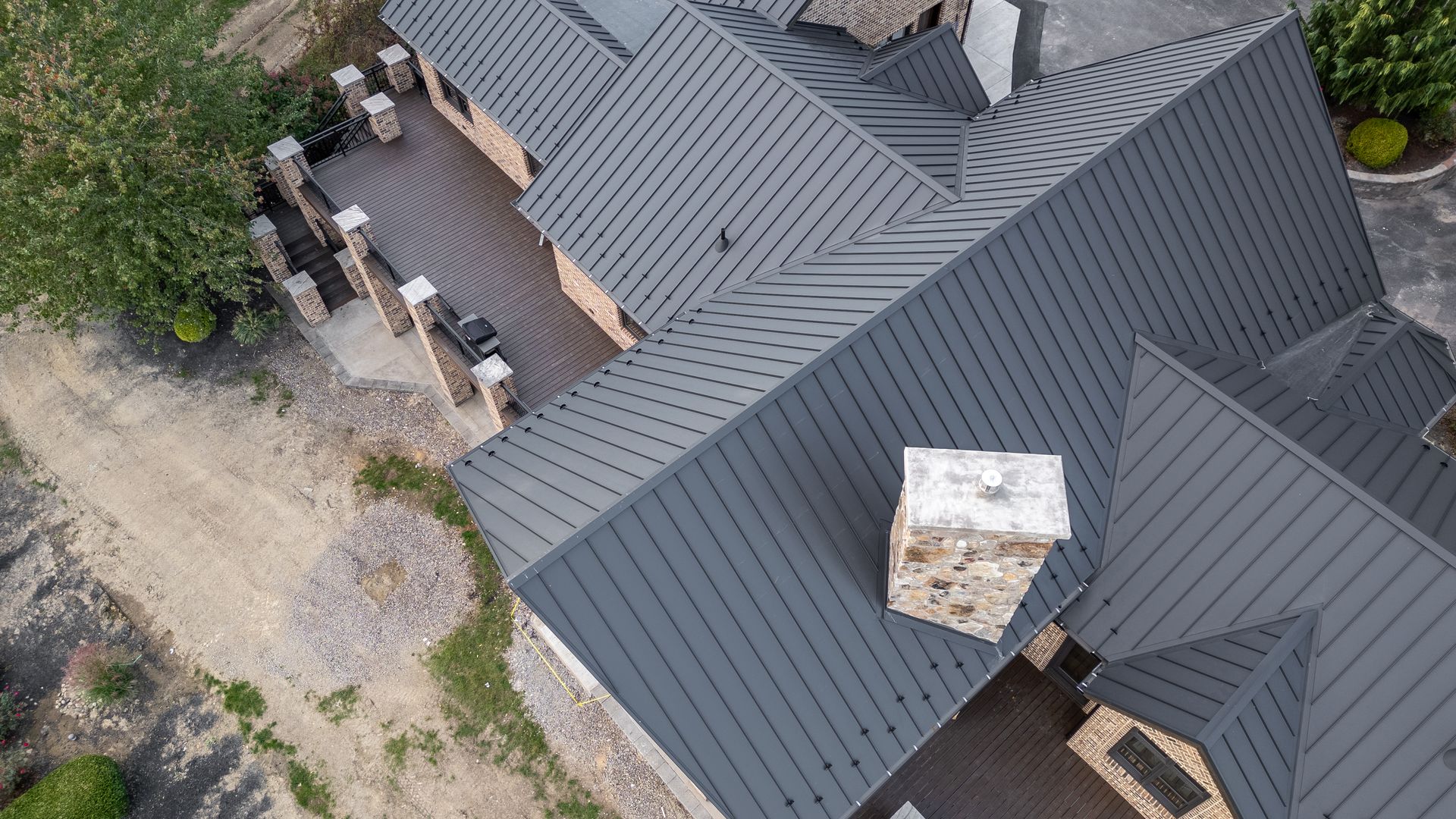 Overhead view of a house with a dark gray metal roof, stone chimney, and deck.