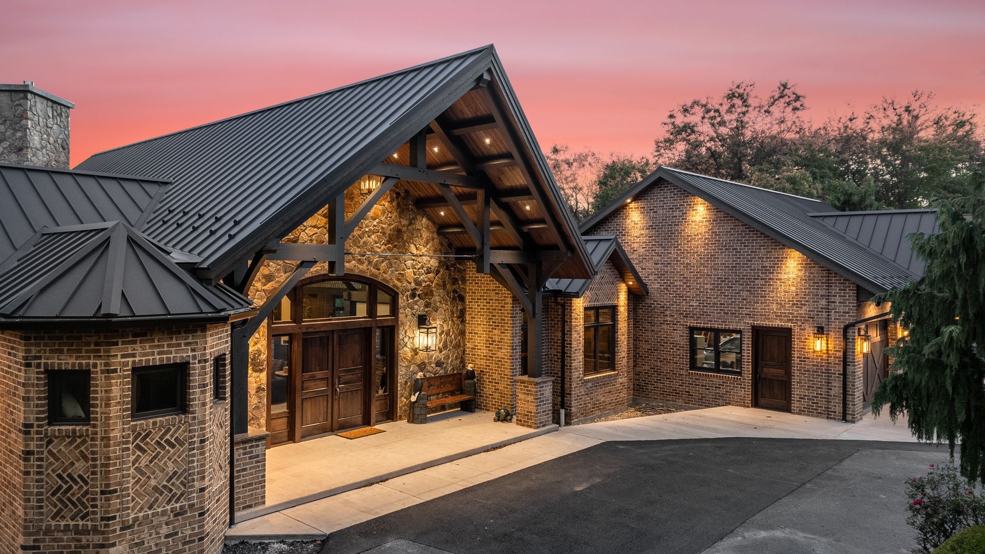 Stone house exterior with dark roof and entryway lit by warm lights against a sunset sky.