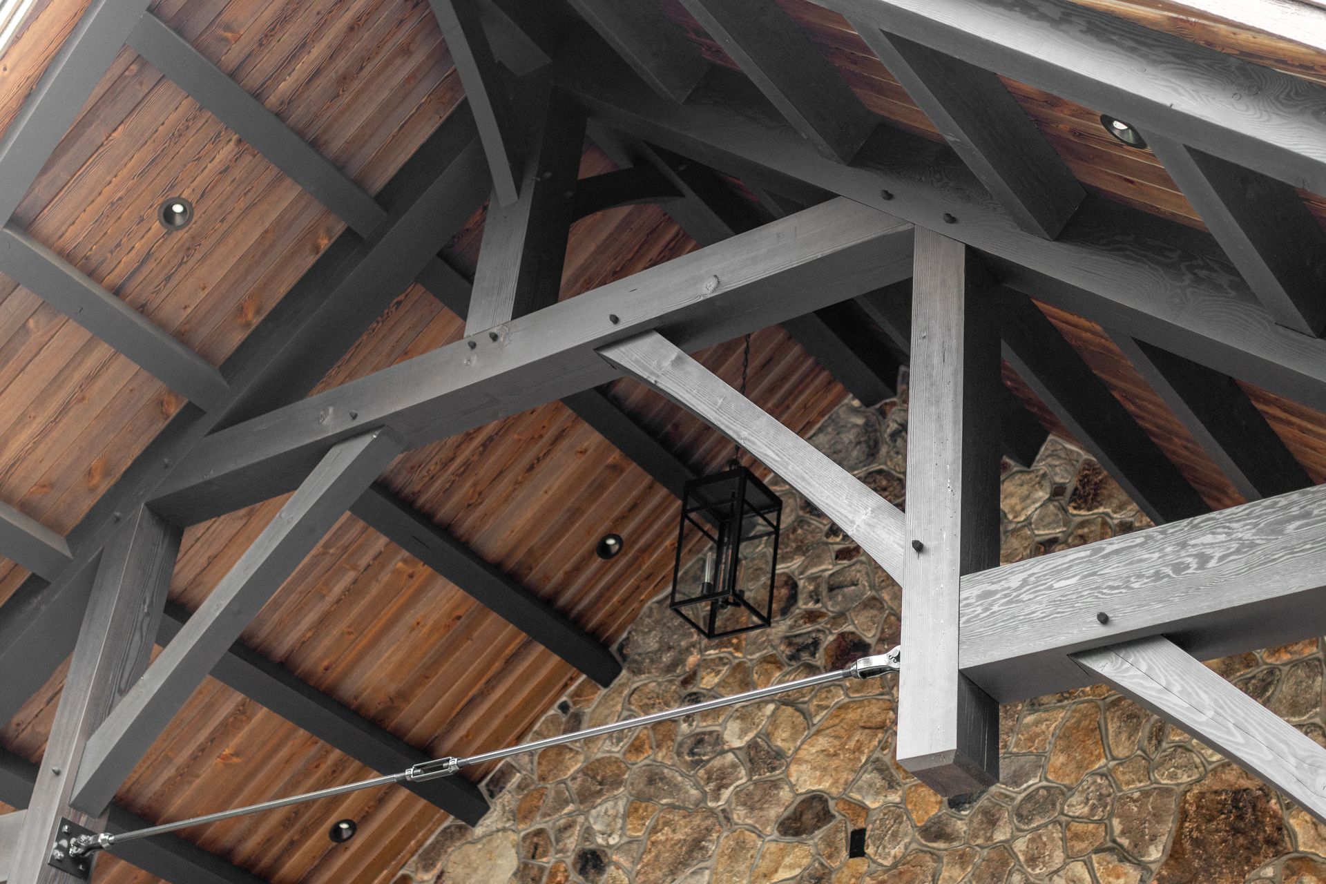 Wooden roof structure with gray beams, brown wooden panels, and a hanging lantern.