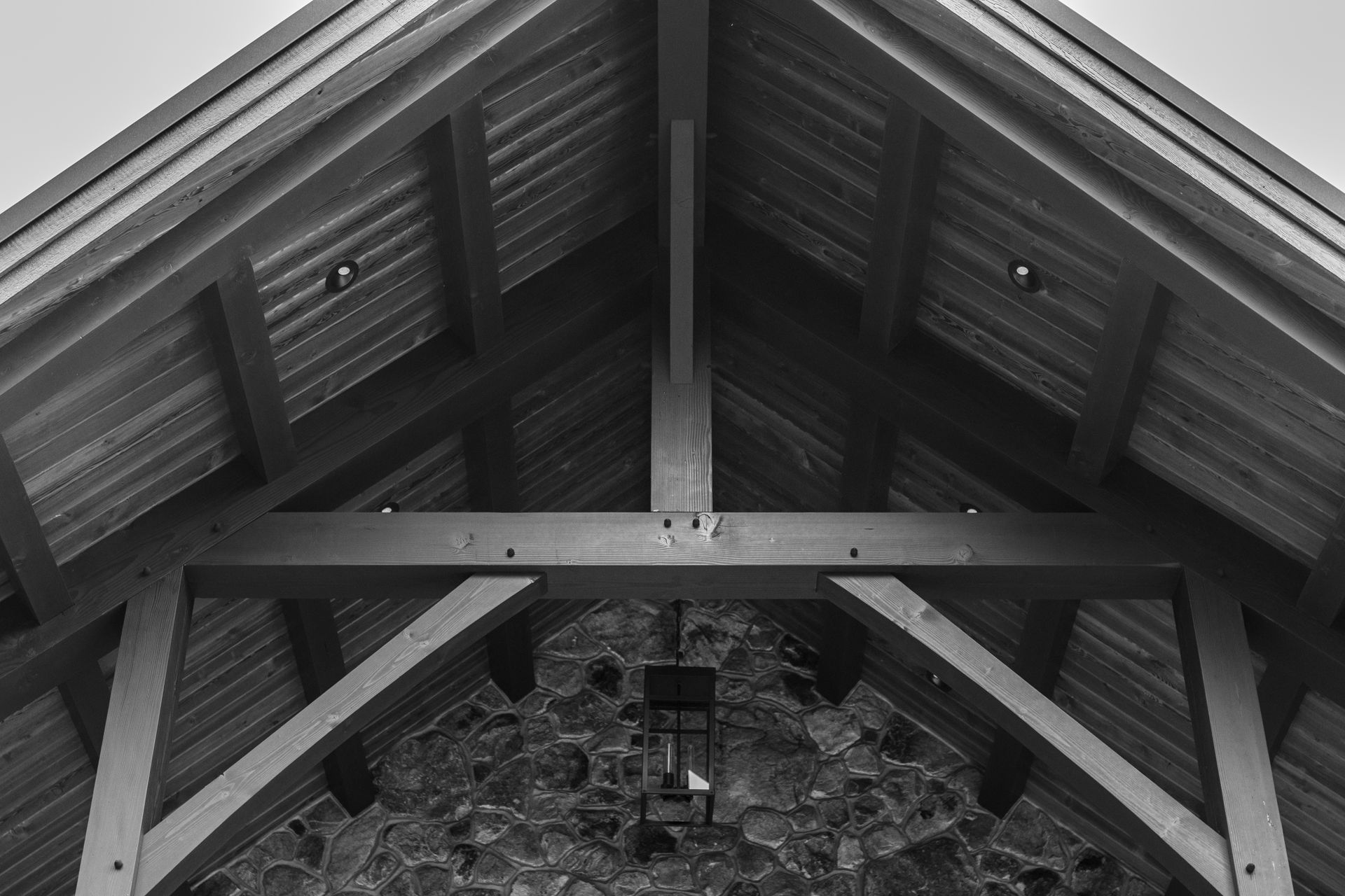 Black and white photo of a wooden roof structure with a stone wall in the background.