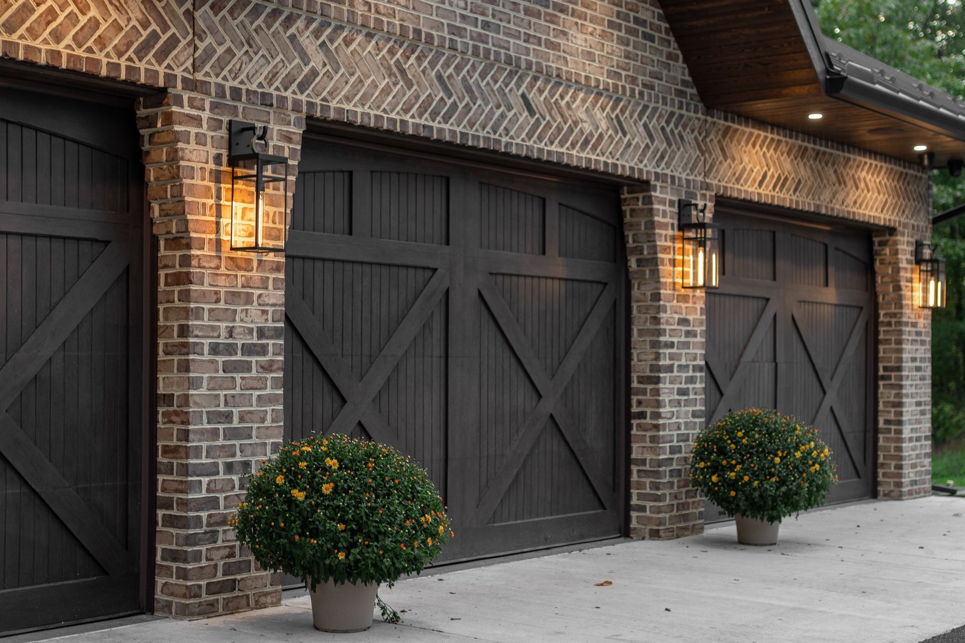 Brick garage with three dark brown doors, each with a decorative X, and two potted plants.