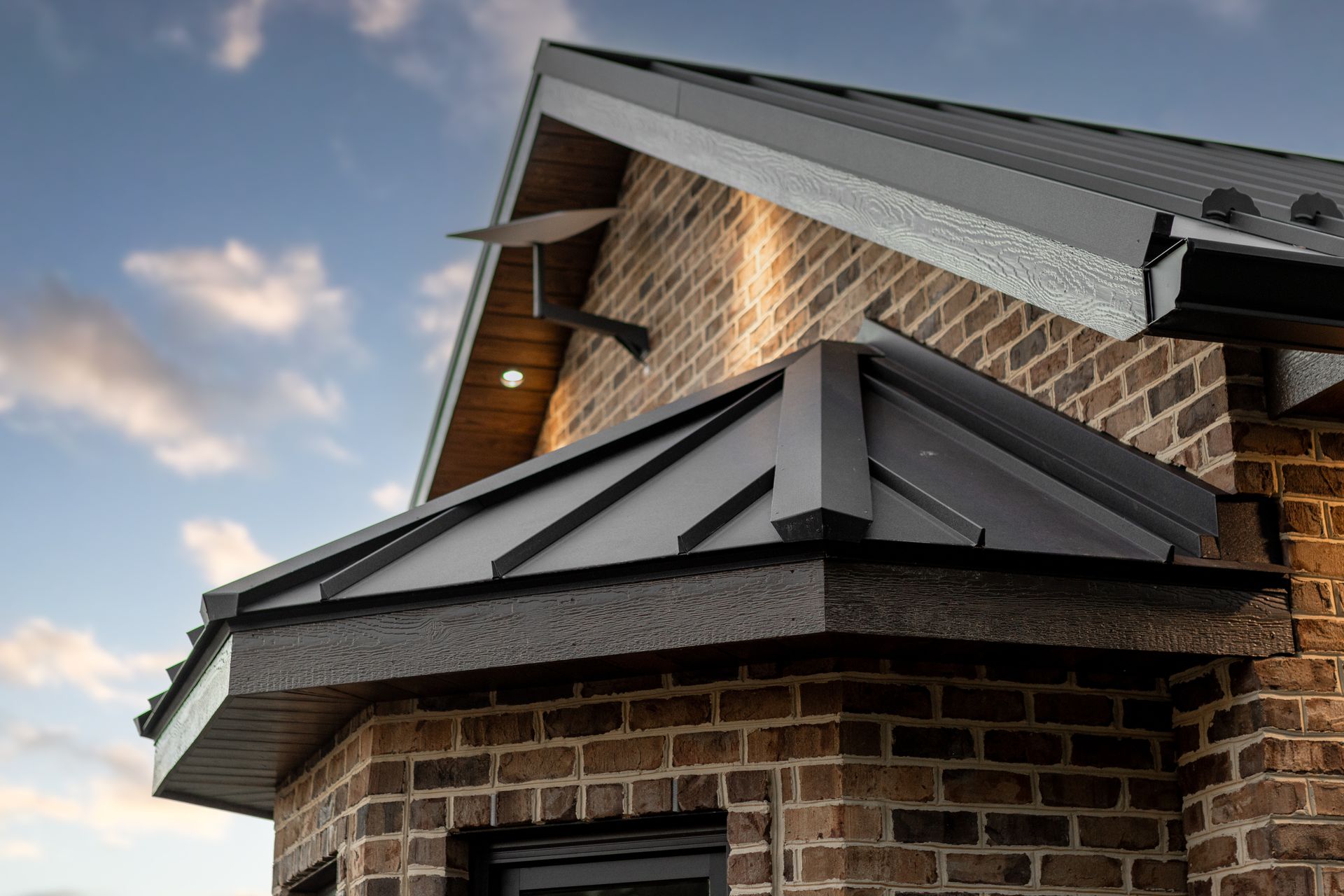 Brick building with a dark metal roof against a cloudy sky.