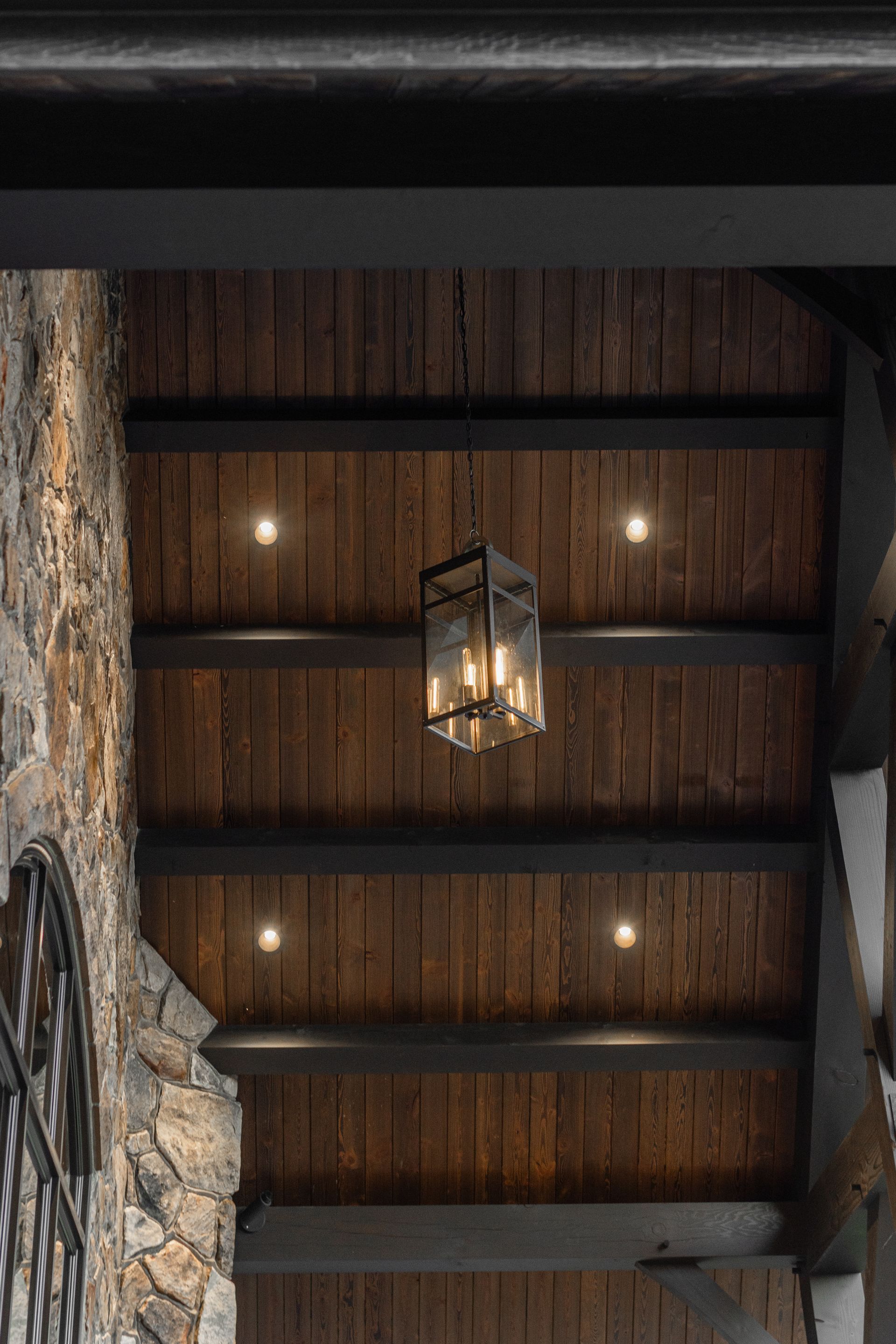 Wooden ceiling with recessed lights and a lantern, part of an outdoor porch.