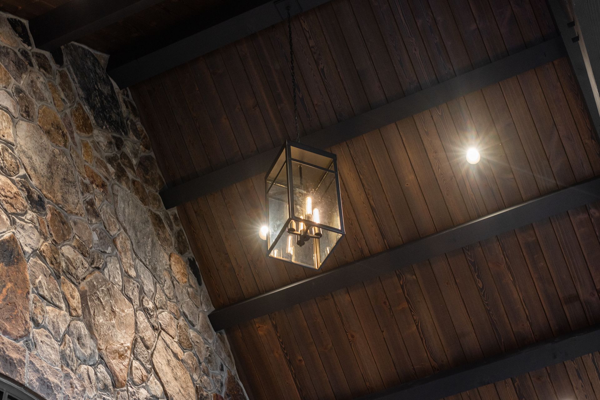 Stone wall, wood ceiling with a hanging lantern and recessed lights.