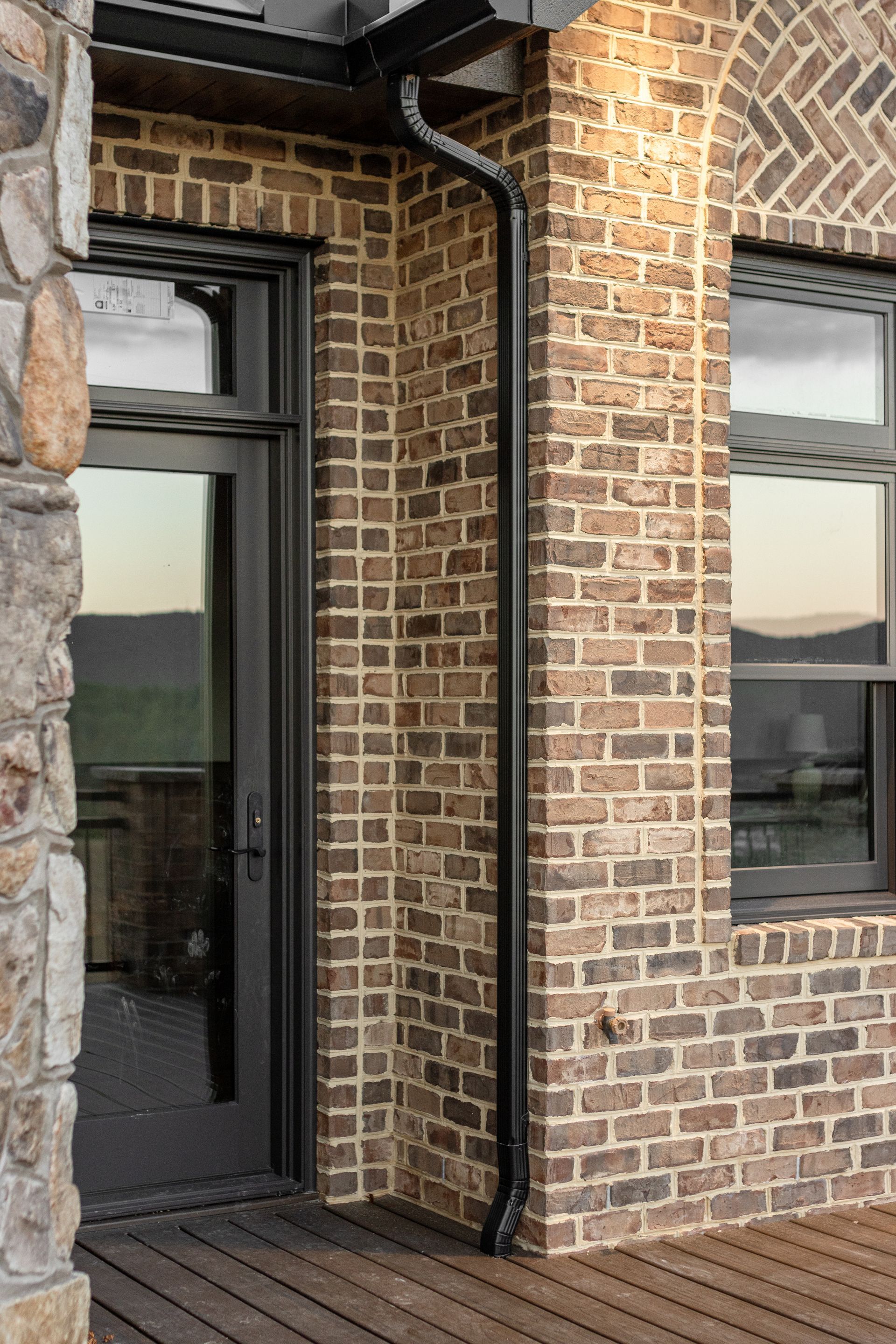 Brick building with dark-framed door, window, and gutter. Wooden deck with a stone column.