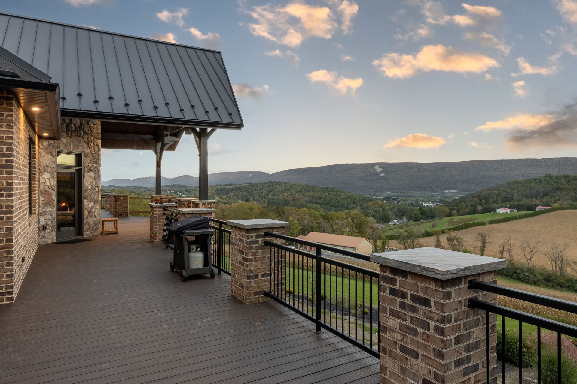 Wooden deck overlooking a valley with mountains. Brick columns and railing, black grill.