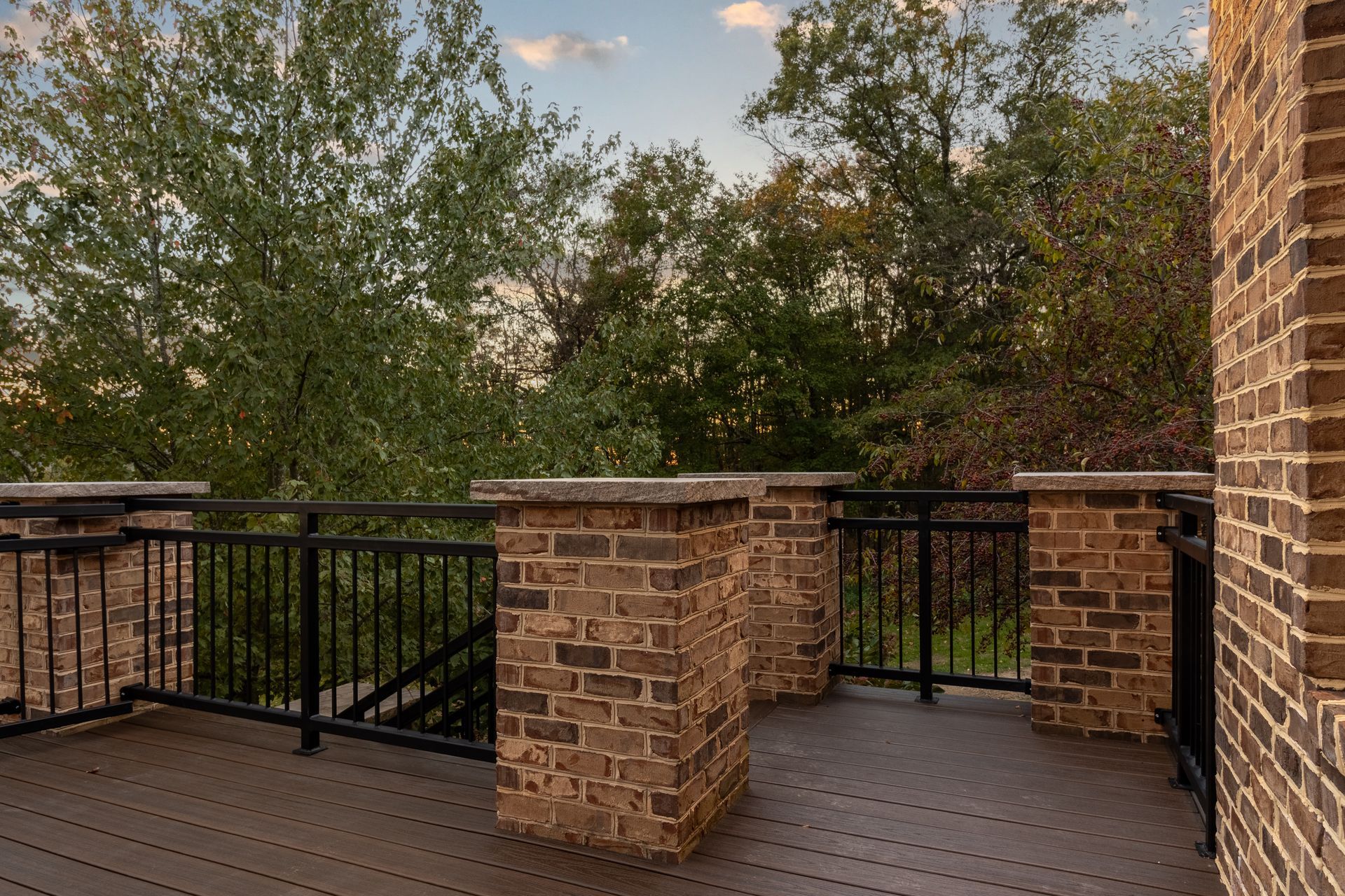 Brick deck with black railing, overlooking trees under a cloudy sky.