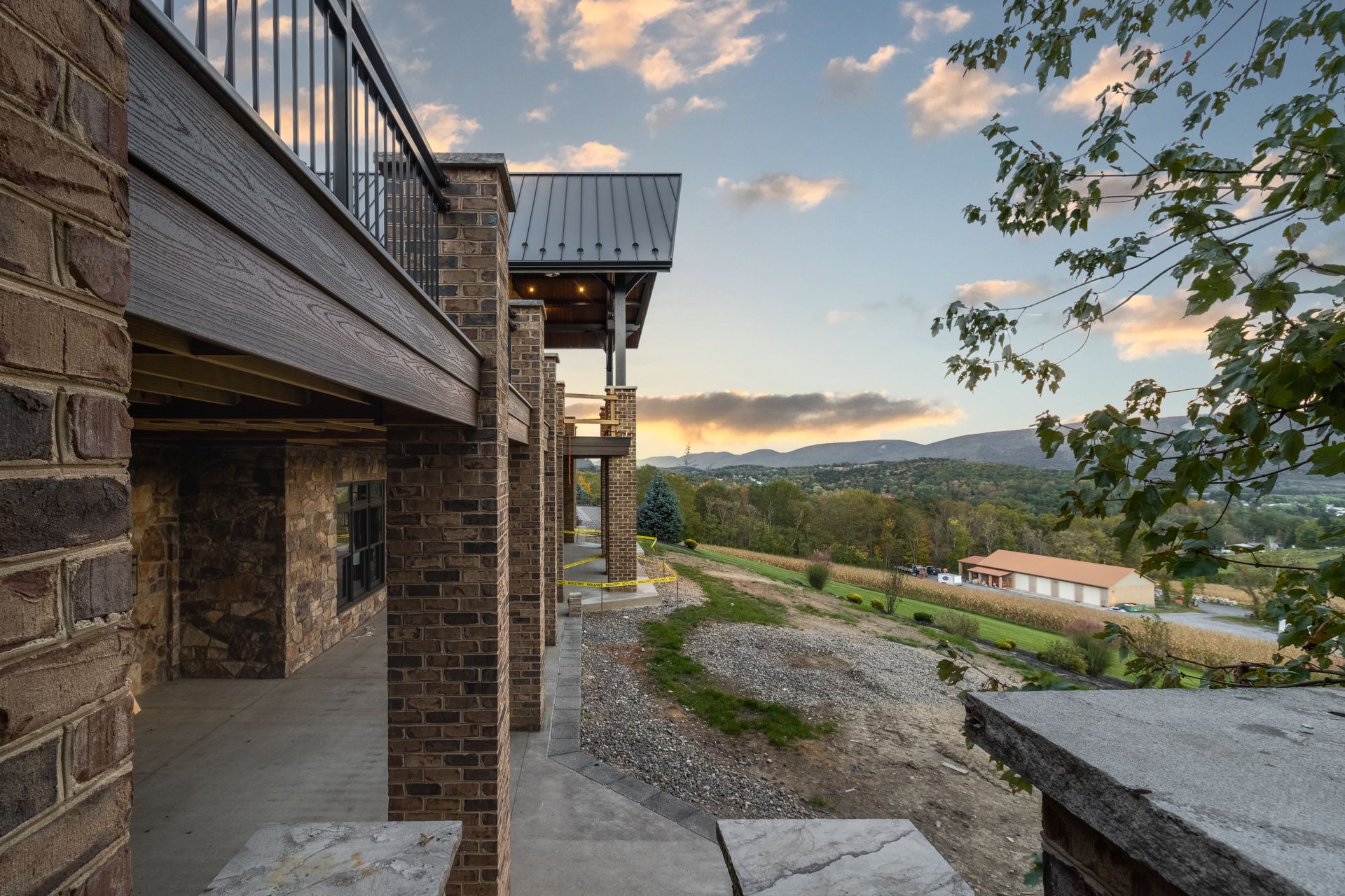 Brick building with a balcony overlooking a valley at dusk; mountains in background.
