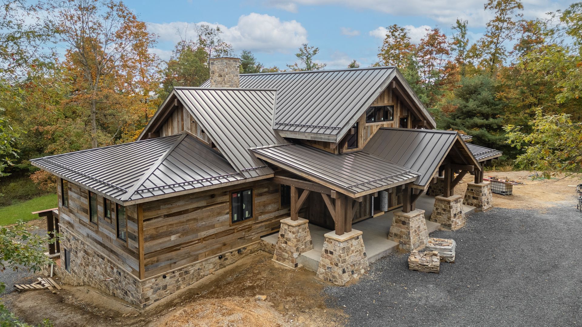 Rustic cabin with stone and wood exterior, metal roof, and porch, surrounded by trees.