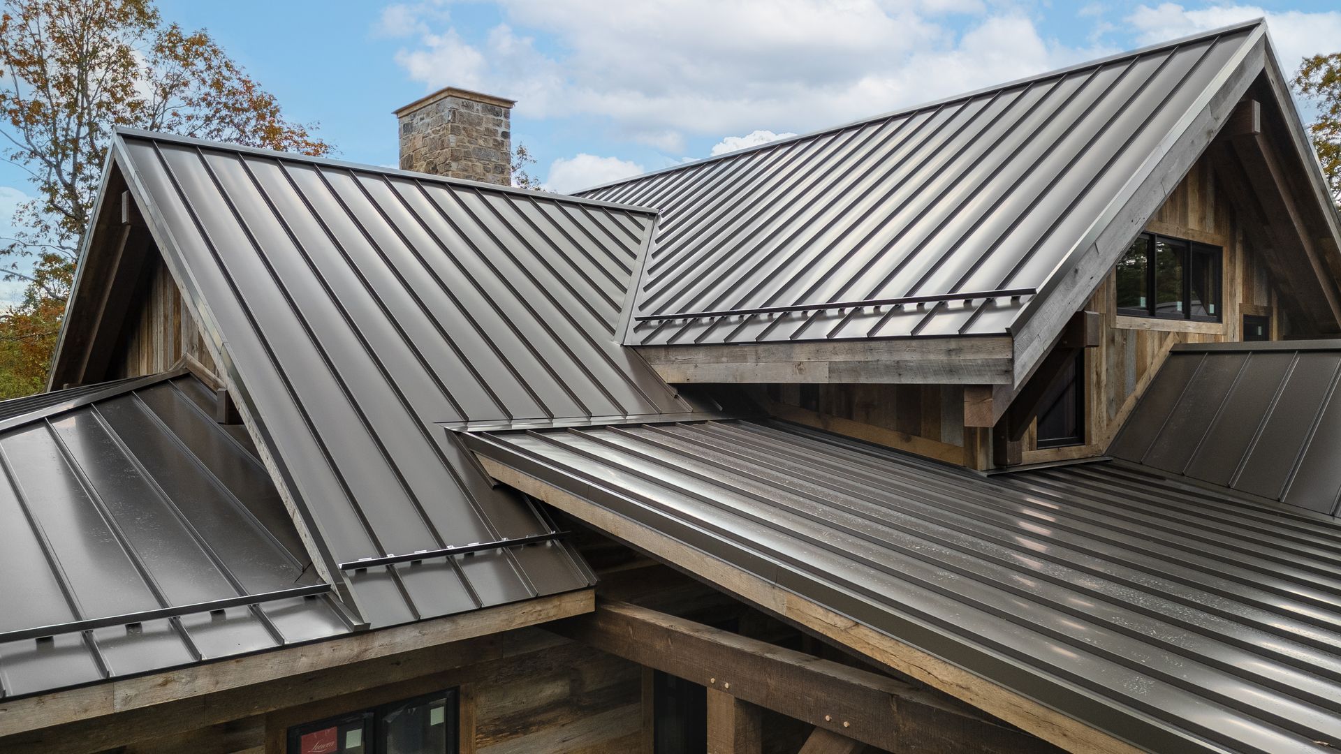 Dark metal roof on a rustic cabin with wooden accents and a stone chimney.