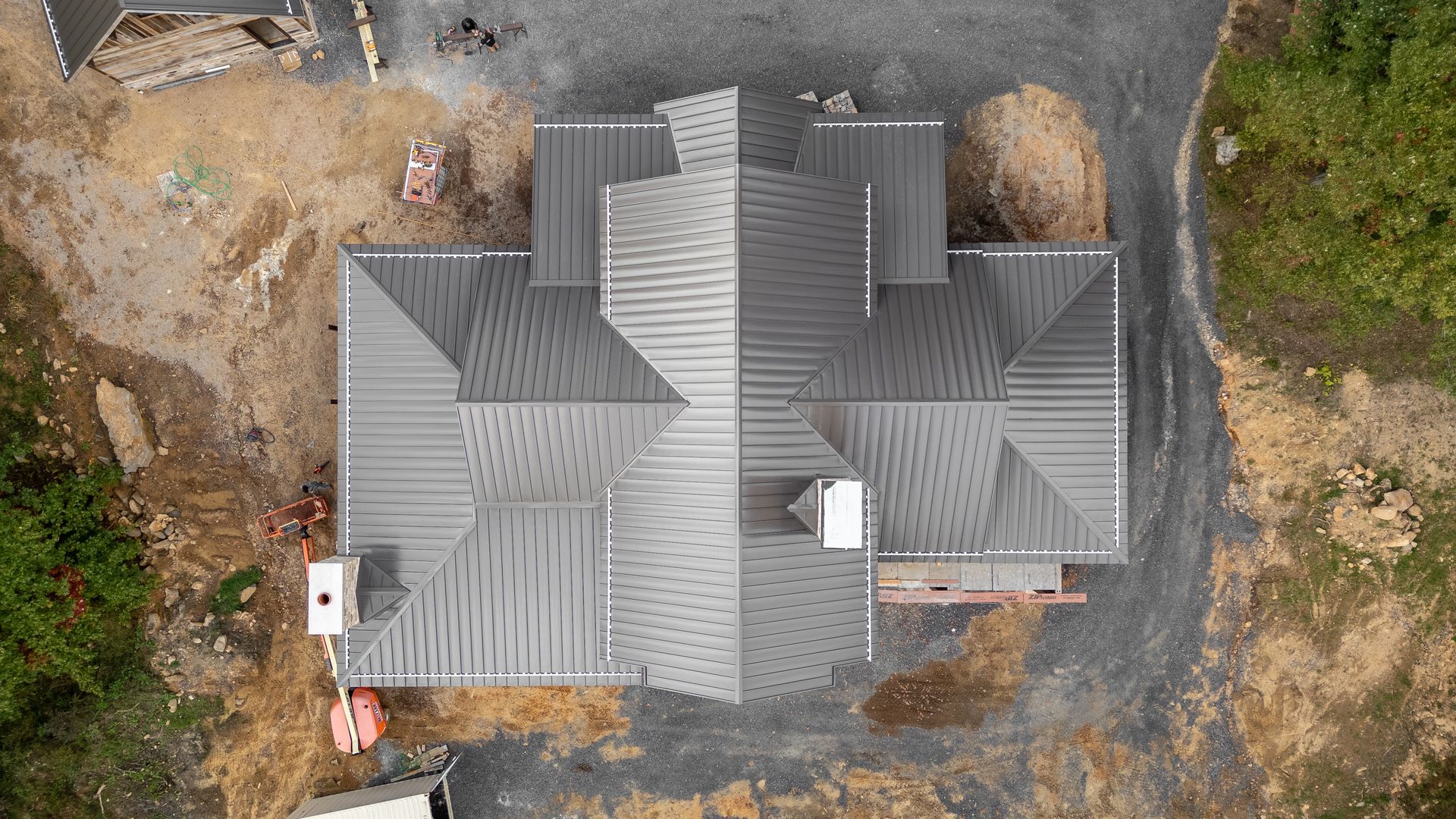 Aerial view of a house under construction with a gray roof, surrounded by gravel and greenery.