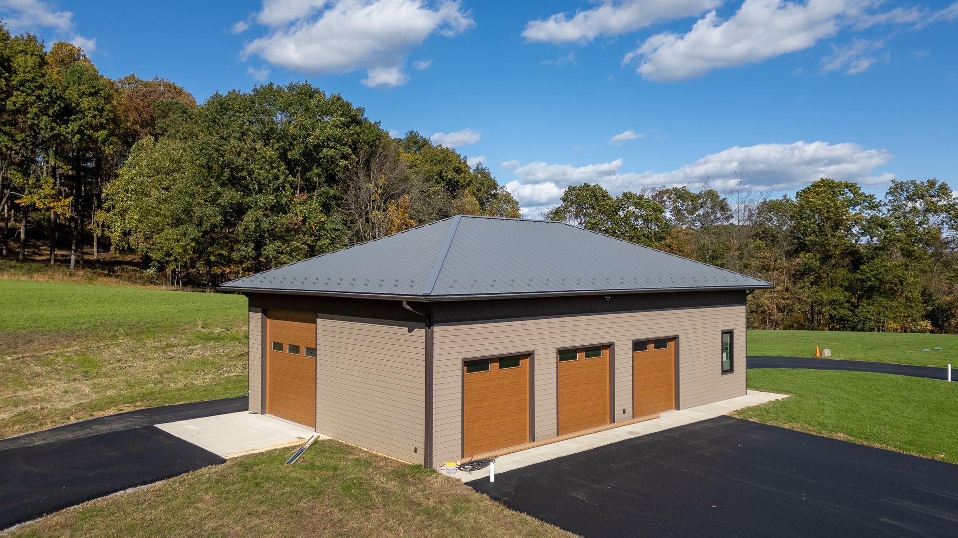 Garage with brown doors, gray roof, and asphalt driveway on a grassy hill under a blue sky.