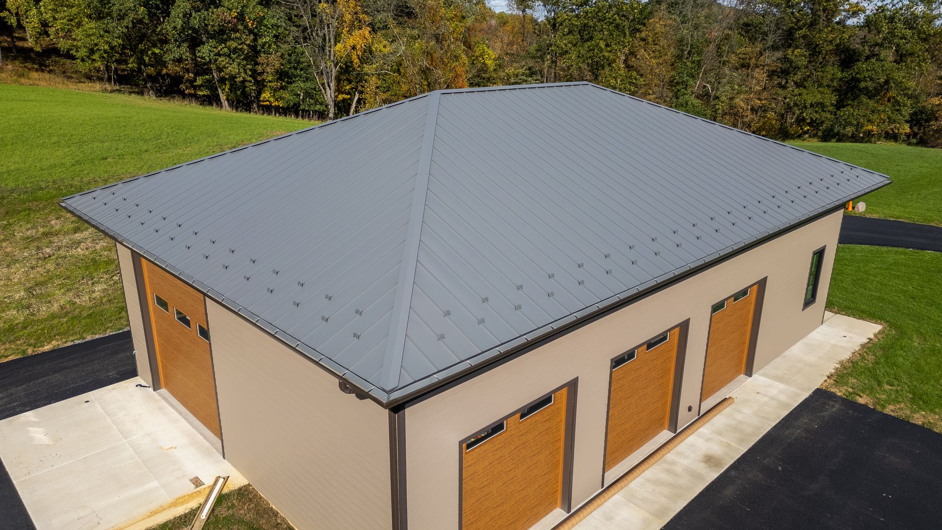 A three-bay garage with a gray metal roof and tan stucco walls, with brown garage doors.