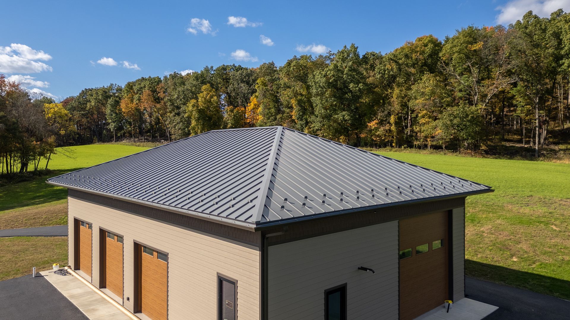 Modern building with gray metal roof, brown doors, and forest backdrop.