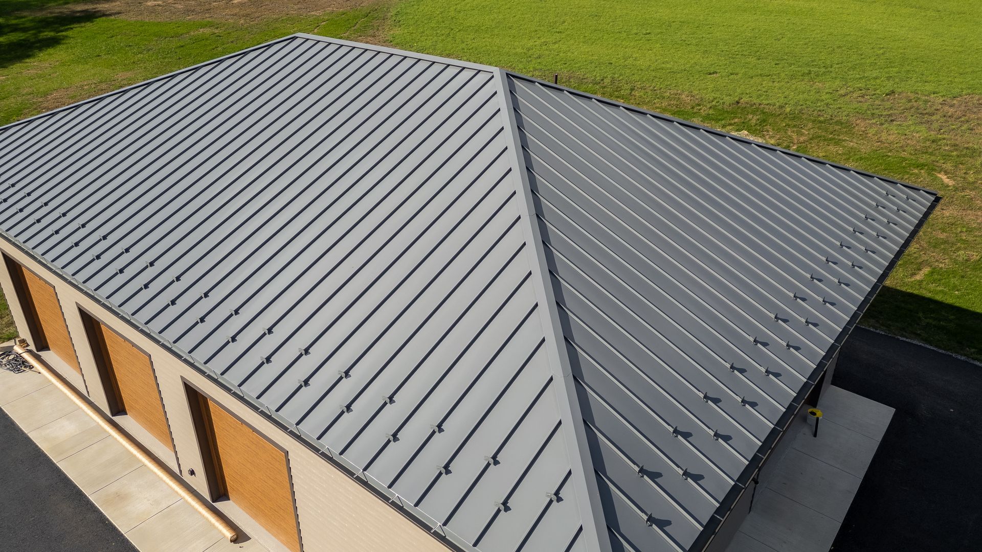 Gray metal roof on a tan building, seen from above with green grass in the background.