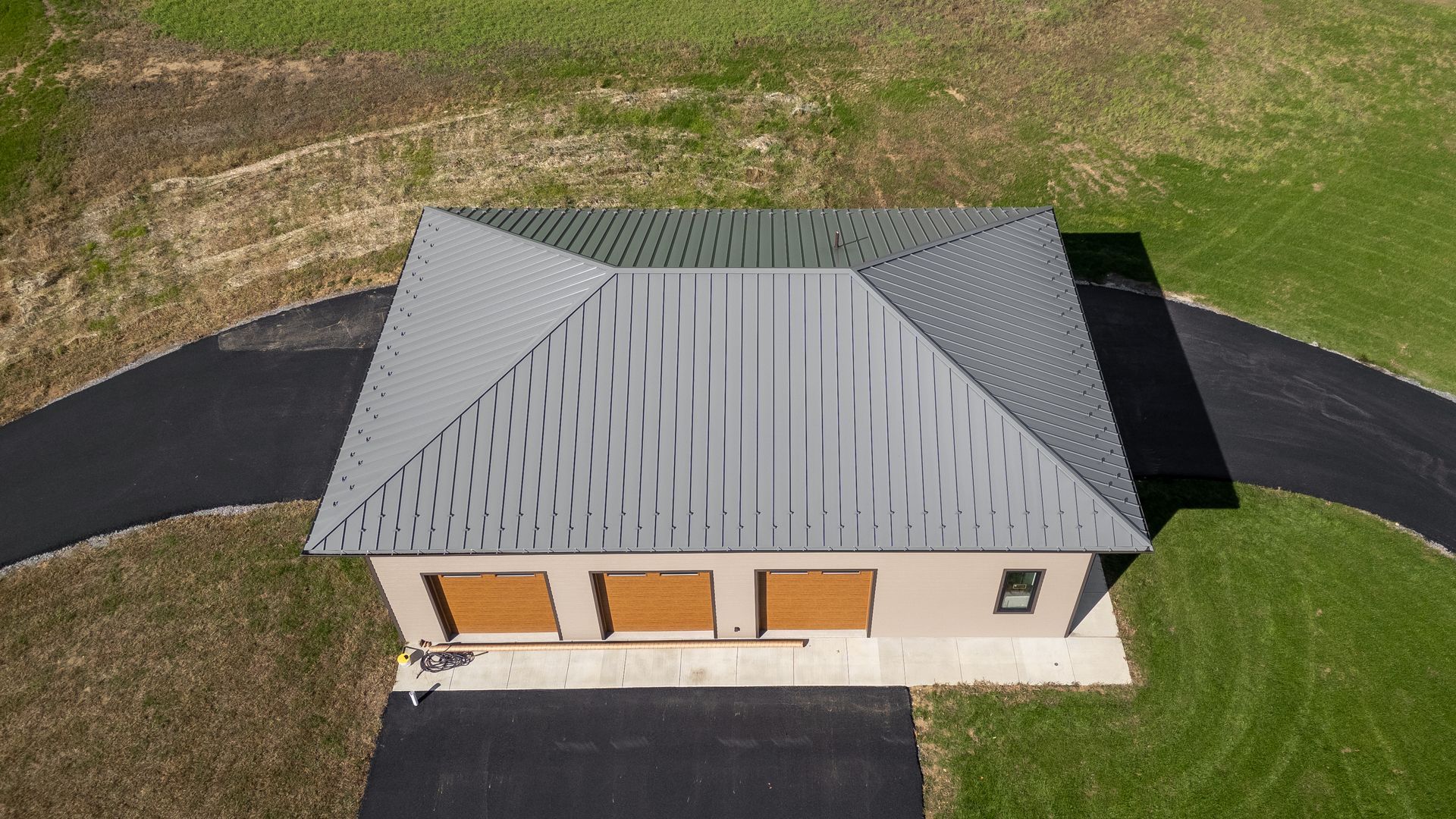 Aerial view of a garage with a dark gray roof, three wooden doors, and a black driveway.