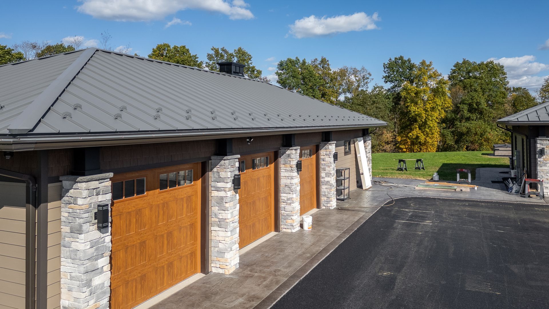 Exterior view of a building with gray metal roof, brown garage doors, and stone accents, on a sunny day.