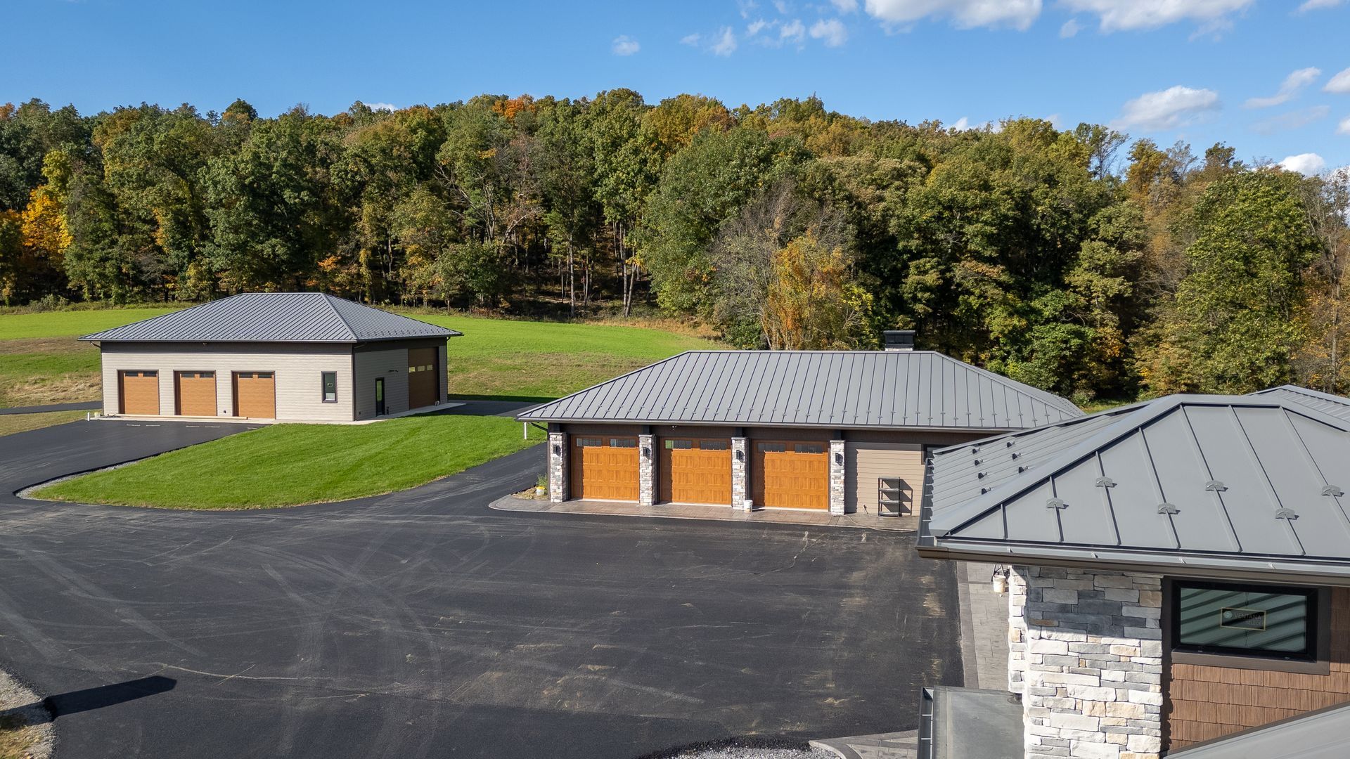 Three tan garages with gray roofs, surrounded by asphalt, grass, and trees.