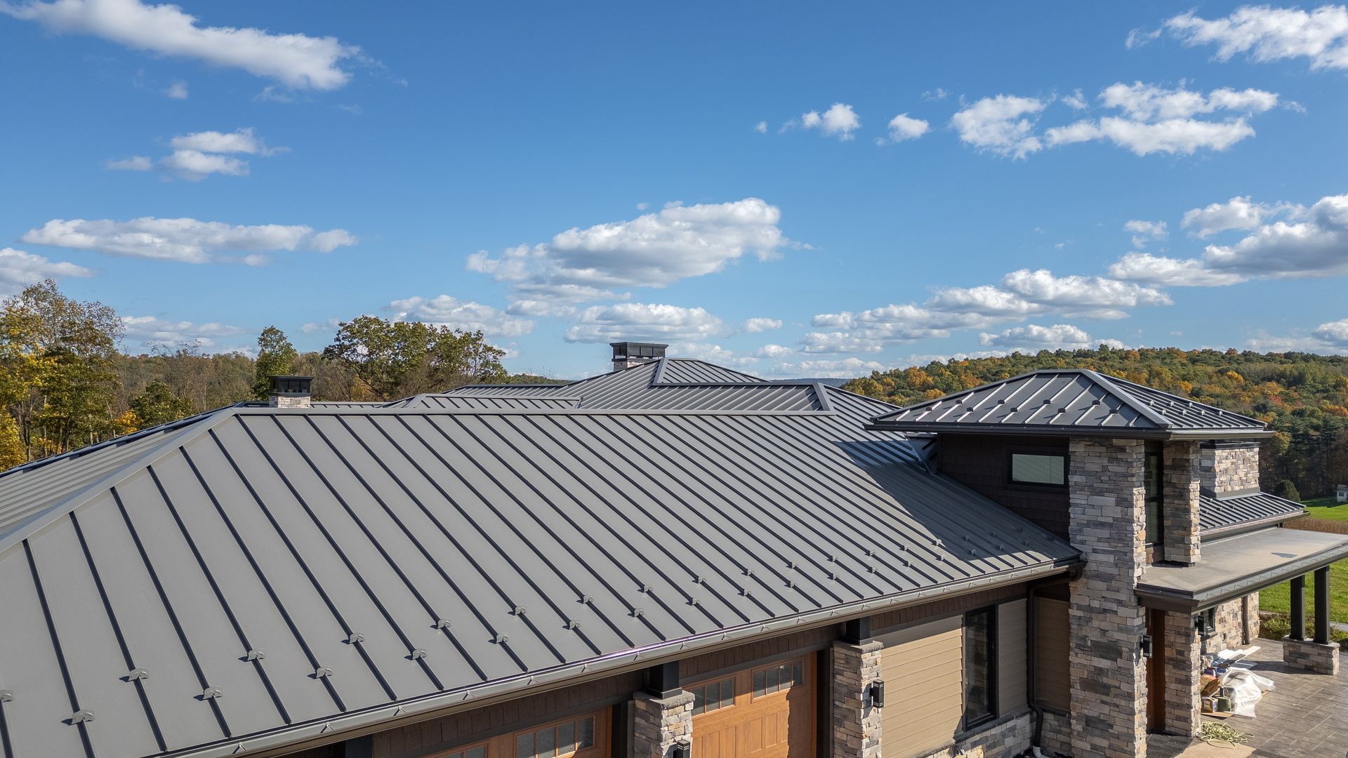Gray metal roof on a large house under a blue sky with clouds.