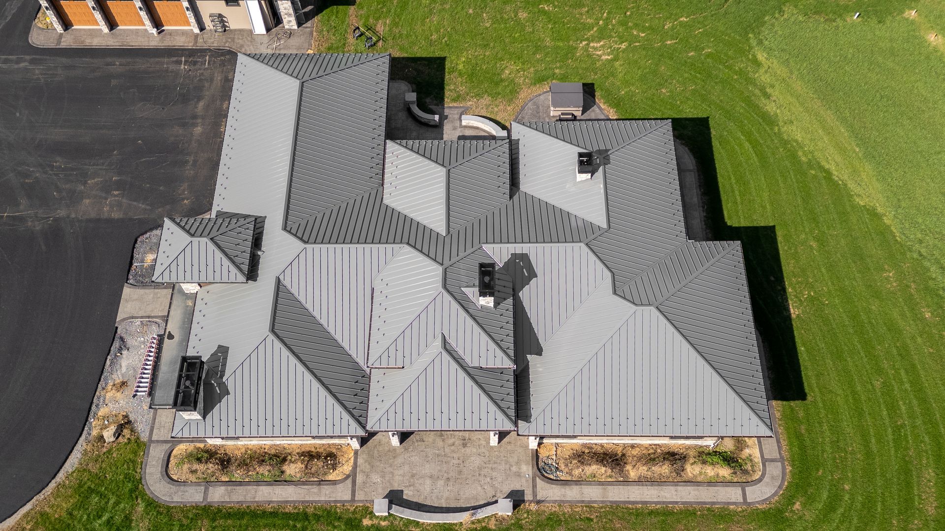 Aerial view of a gray-roofed house on a green lawn, with a black driveway and a stone walkway.