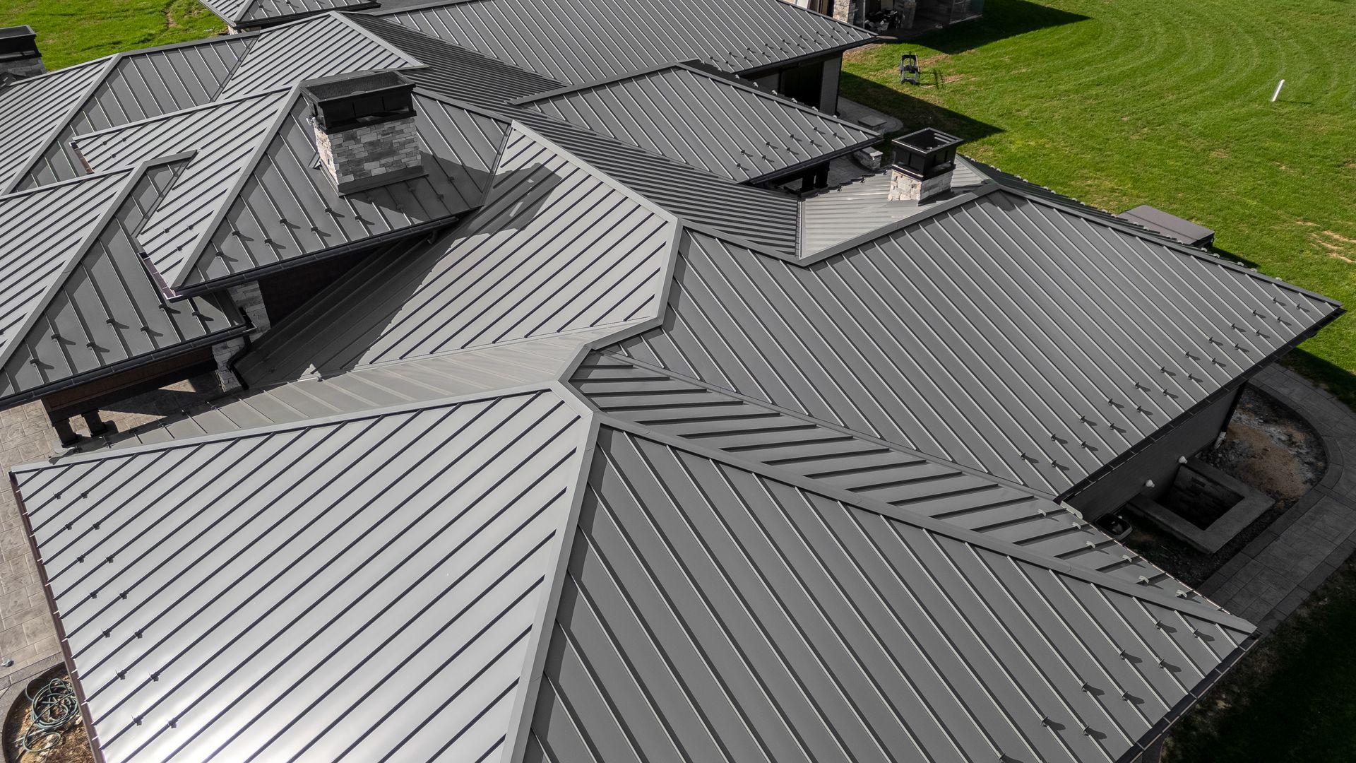 Gray metal roof on a house with multiple gables and chimneys, surrounded by green grass.