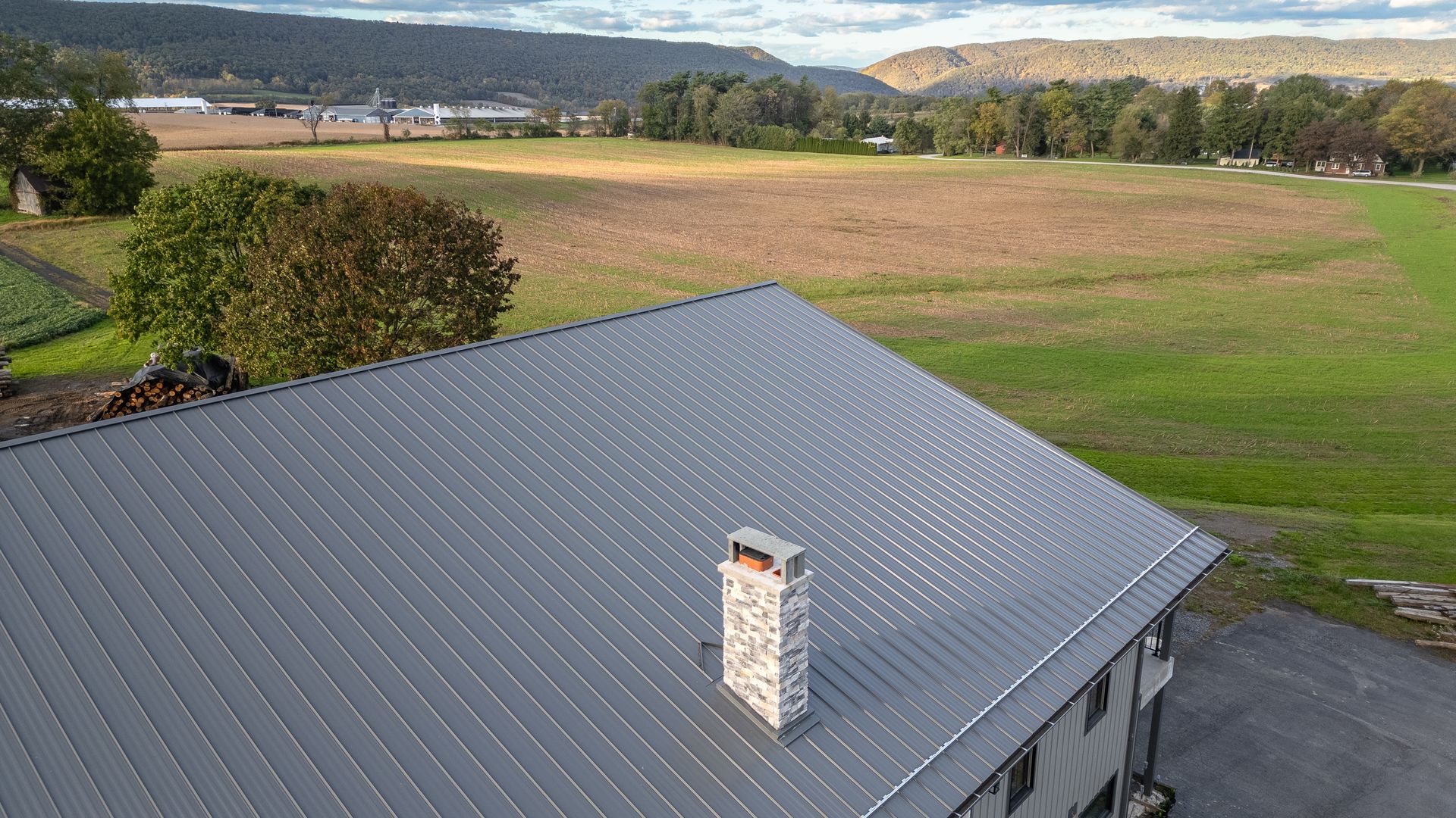 Gray metal roof with stone chimney, overlooking fields and mountains.