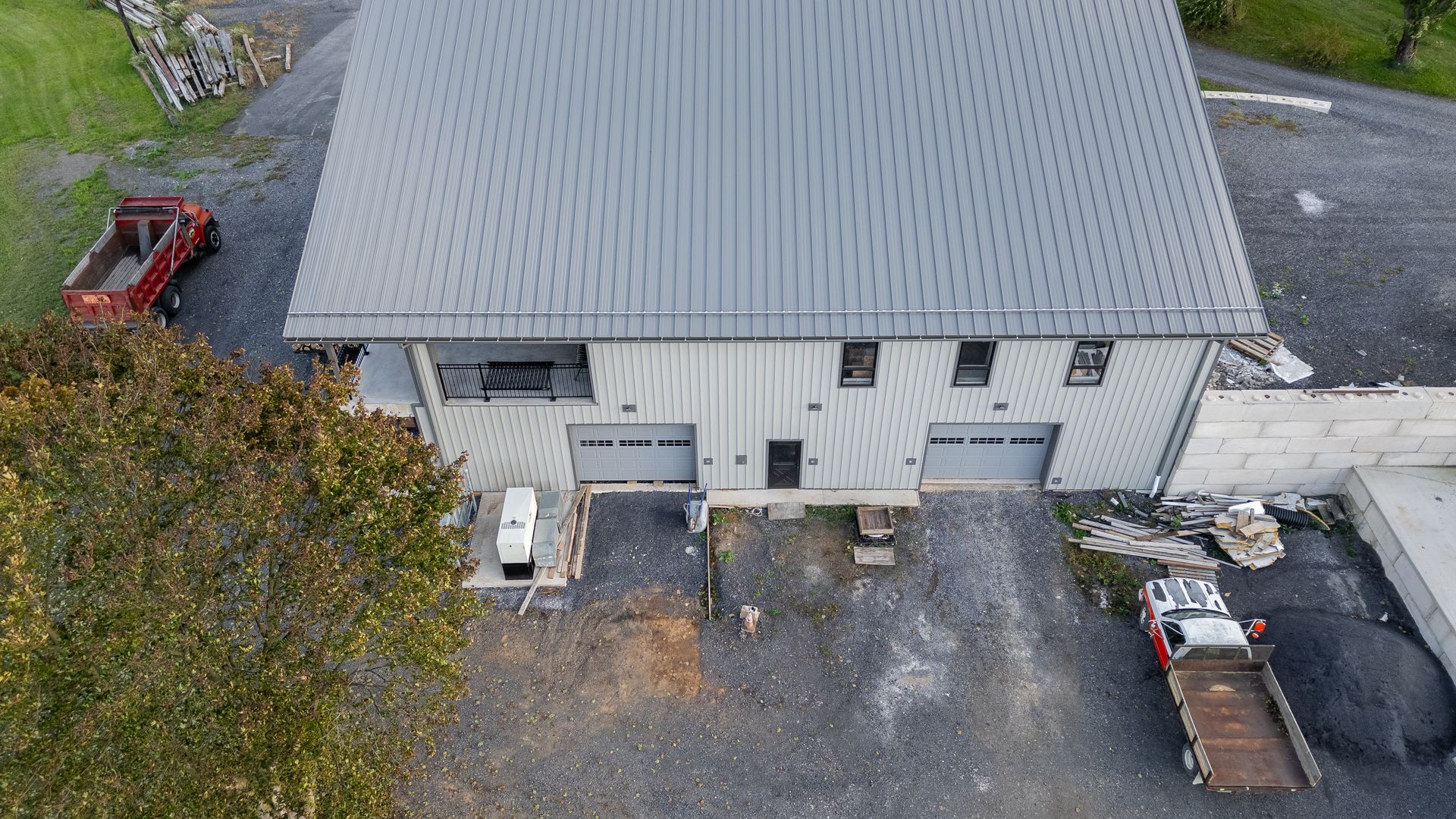 Overhead view of a building with gray metal roof and siding, two garage doors, and construction vehicles.