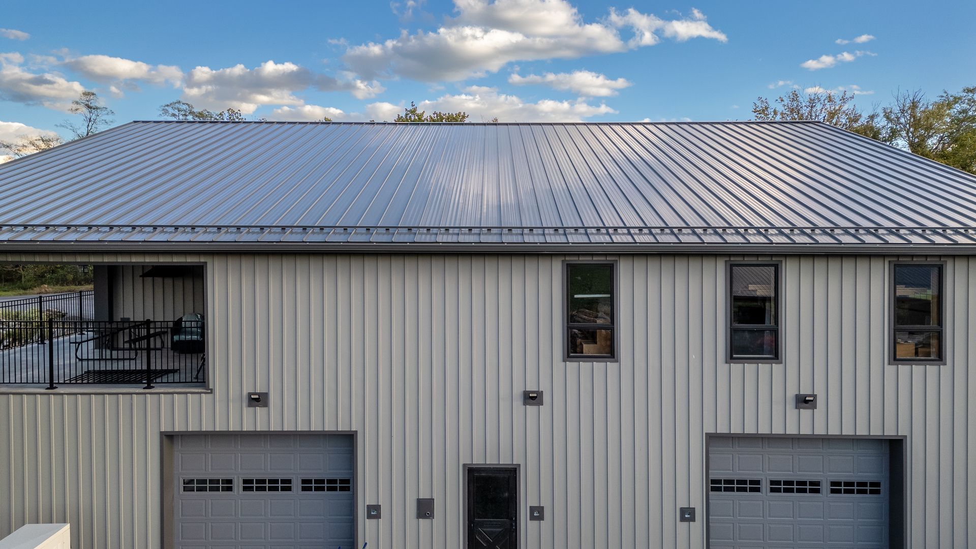 Silver metal-roofed building with white siding, garage doors, and windows against a cloudy sky.