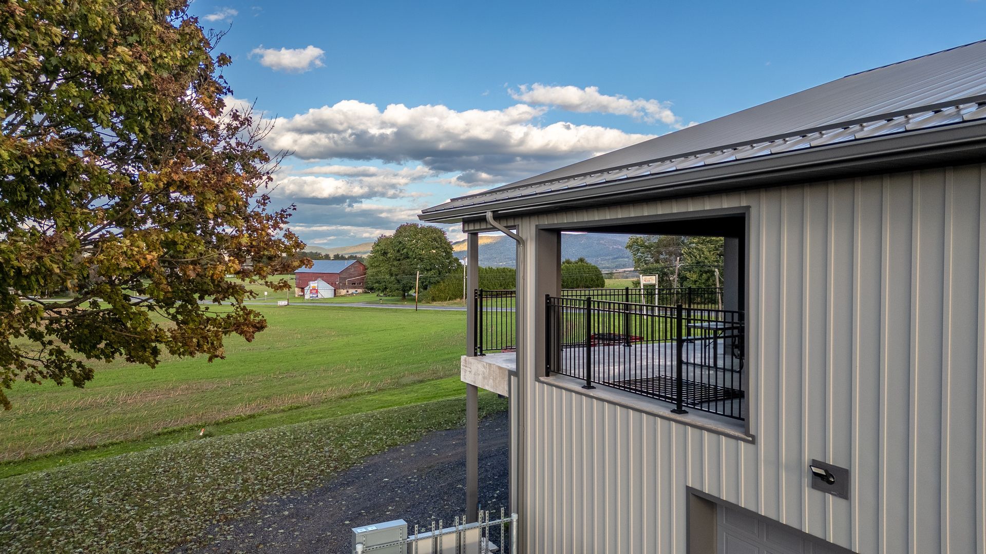 Exterior of a modern building with a balcony overlooking a green field and distant red barn.