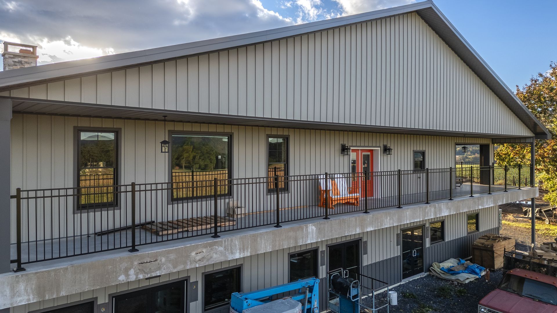 Two-story building with grey siding, black railing, and a red door. Cloudy sky in background.