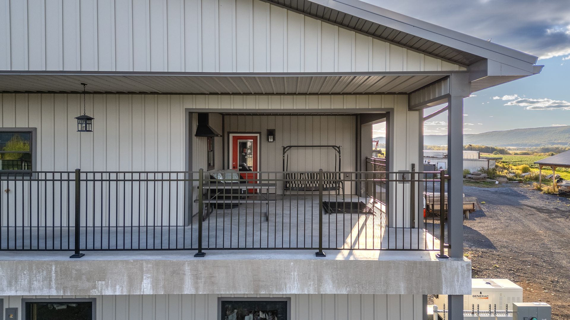 Gray house with black railing balcony, red door, and scenic view.
