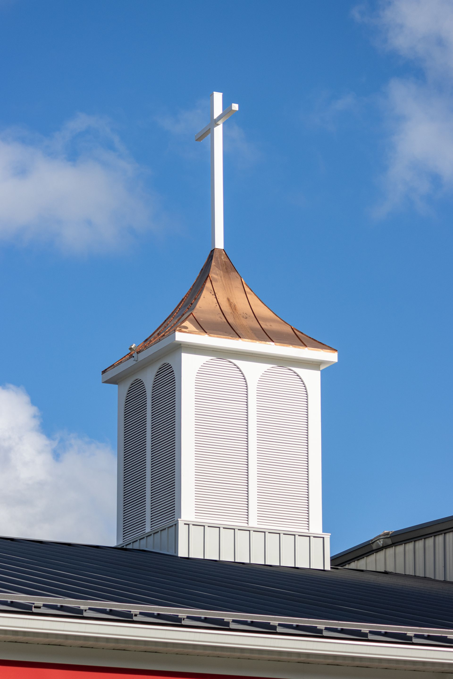White church steeple with copper roof and cross, blue sky.