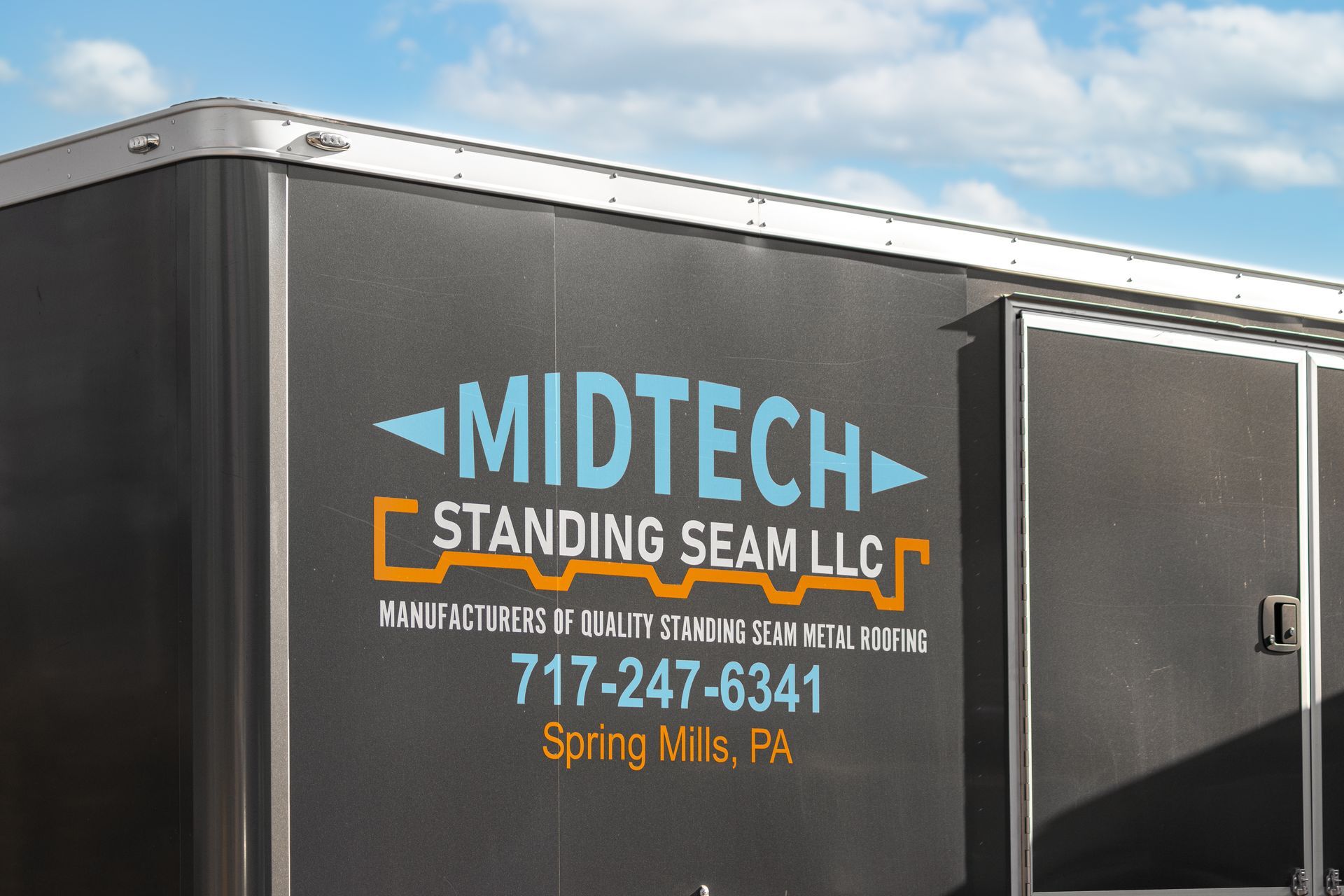 Midtech Standing Seam LLC logo on a dark trailer with the company's phone number and location, Spring Mills, PA.