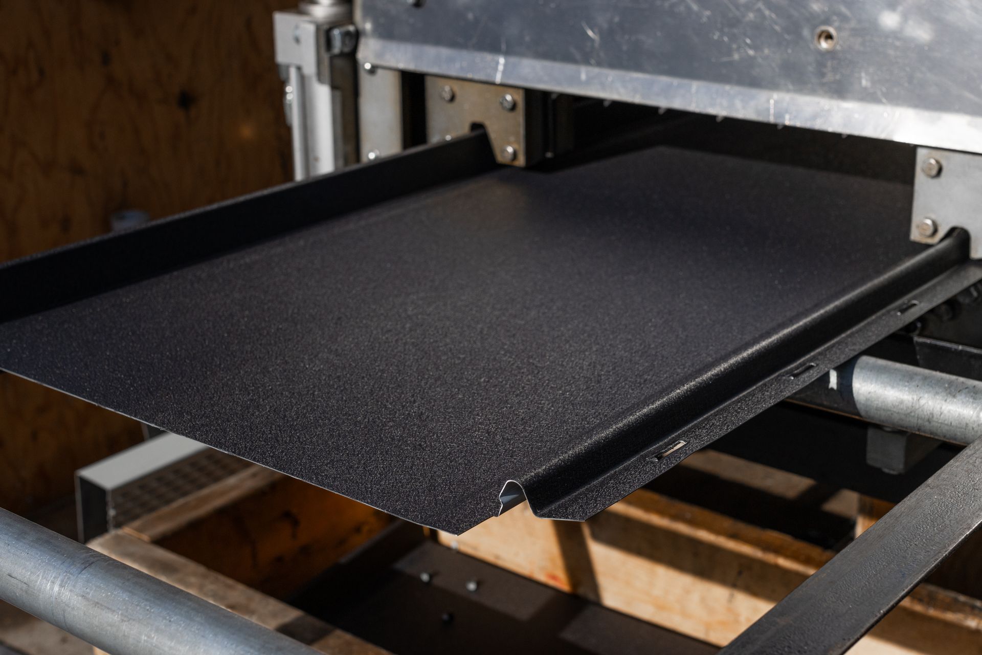 Black metal sheet being formed by a machine. Industrial setting.