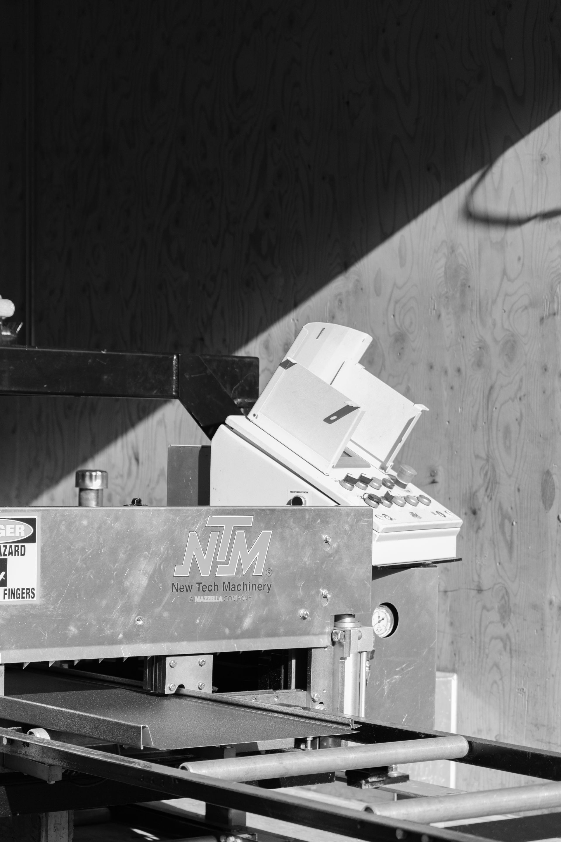 A metal industrial machine against a wooden wall. Sunlight casts a diagonal shadow.