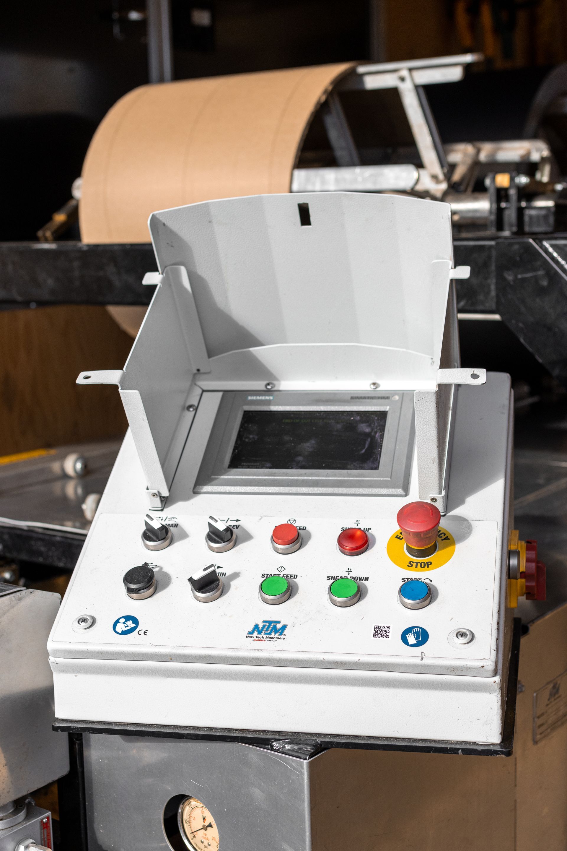 Control panel with buttons, a screen, and a red emergency stop button on industrial machinery.